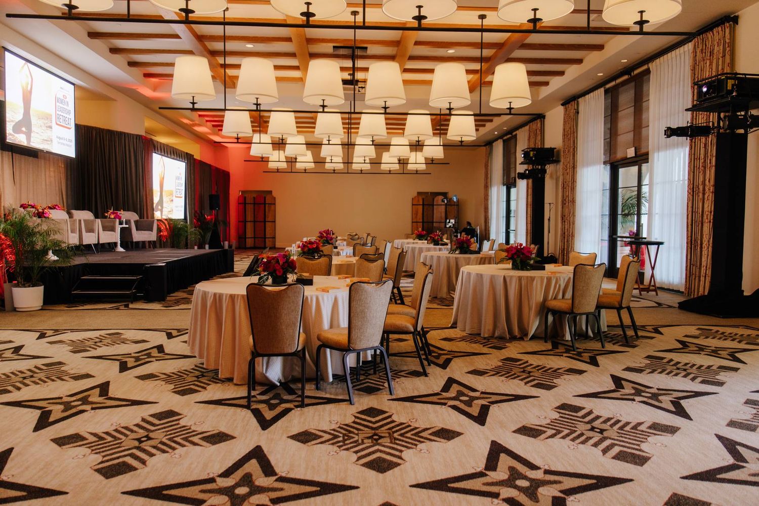 Elegant banquet hall with round tables, ornate geometric floor, and warm chandelier lighting set for a formal event.