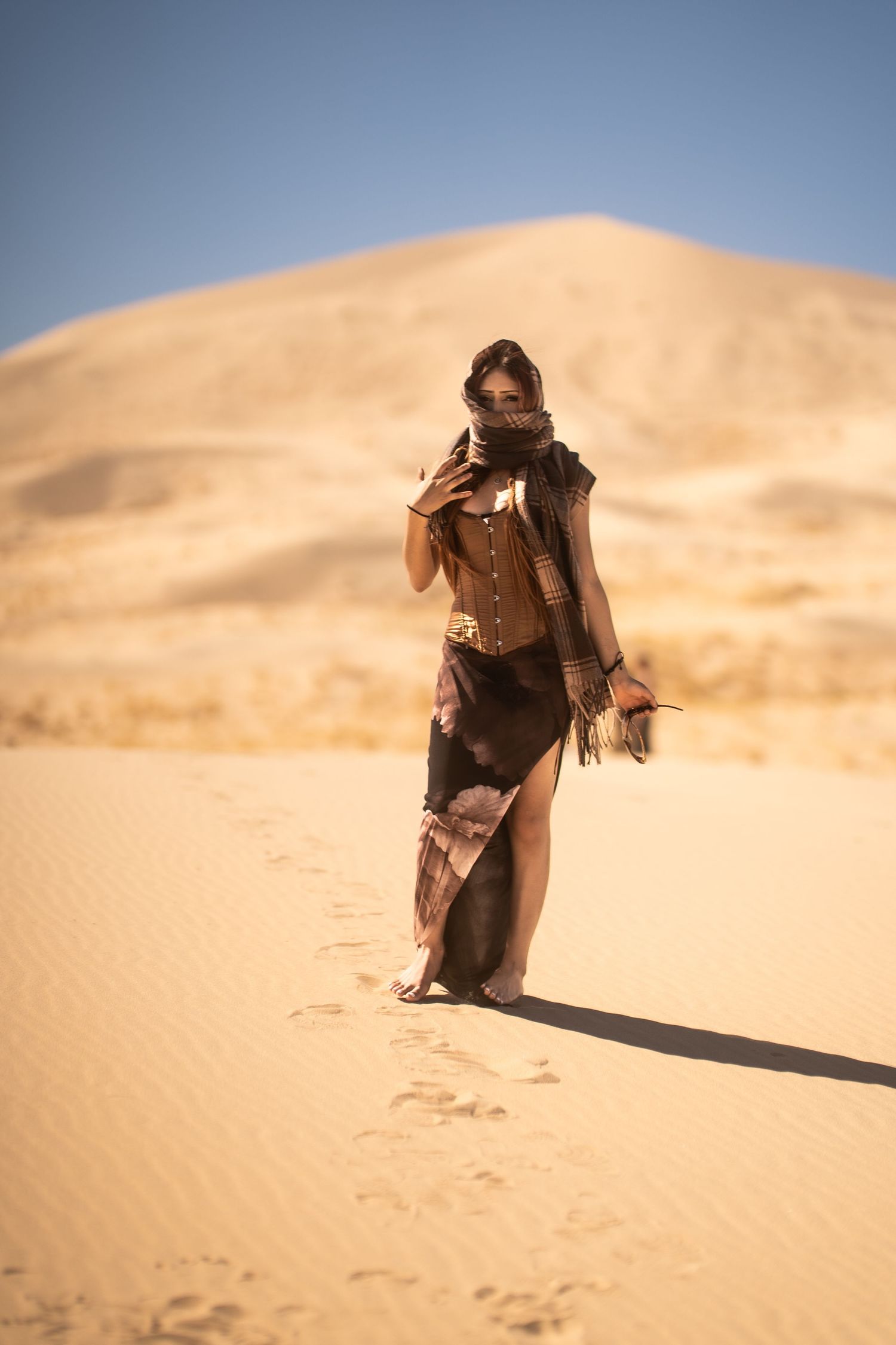 Woman in desert warrior costume walking on sand dunes in bright sunlight.