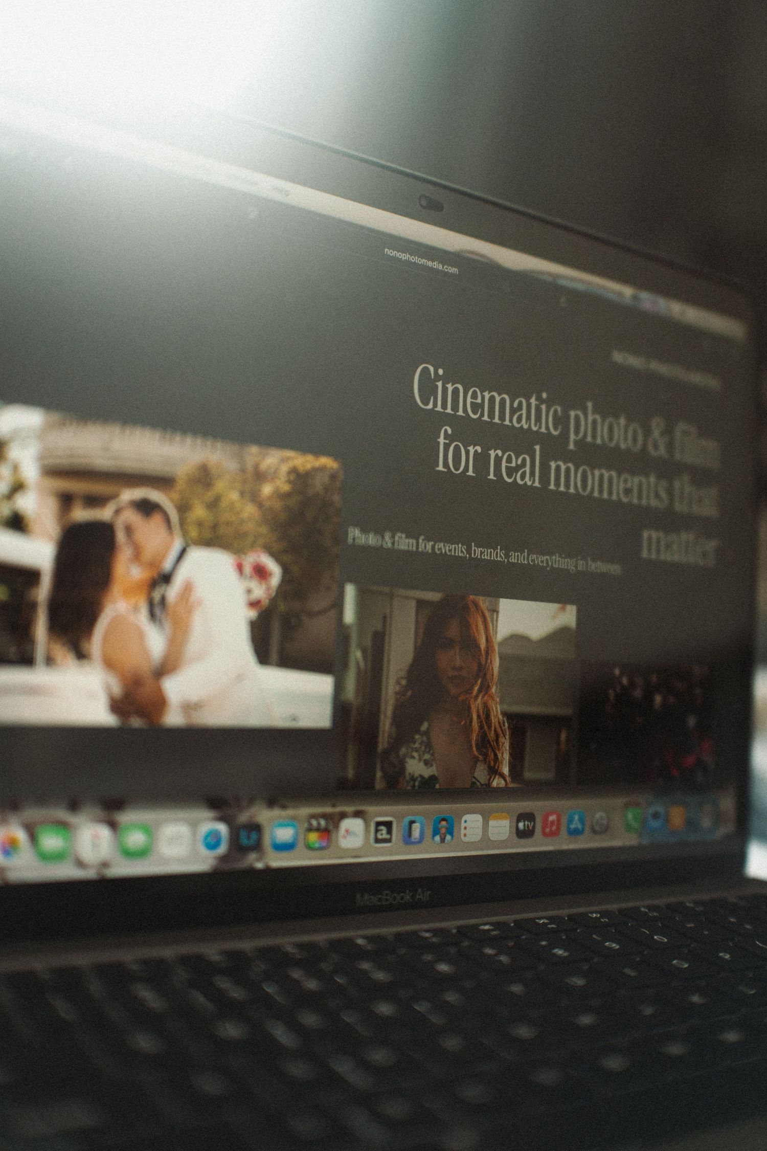 Laptop screen displaying a cinematic wedding photography website with elegant couple photo and tagline about real moments.