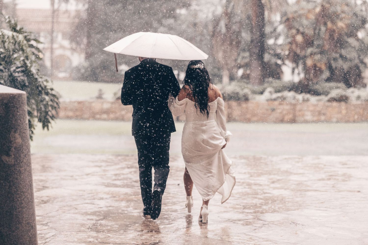A couple walks in heavy rain sharing a white umbrella, viewed from behind.