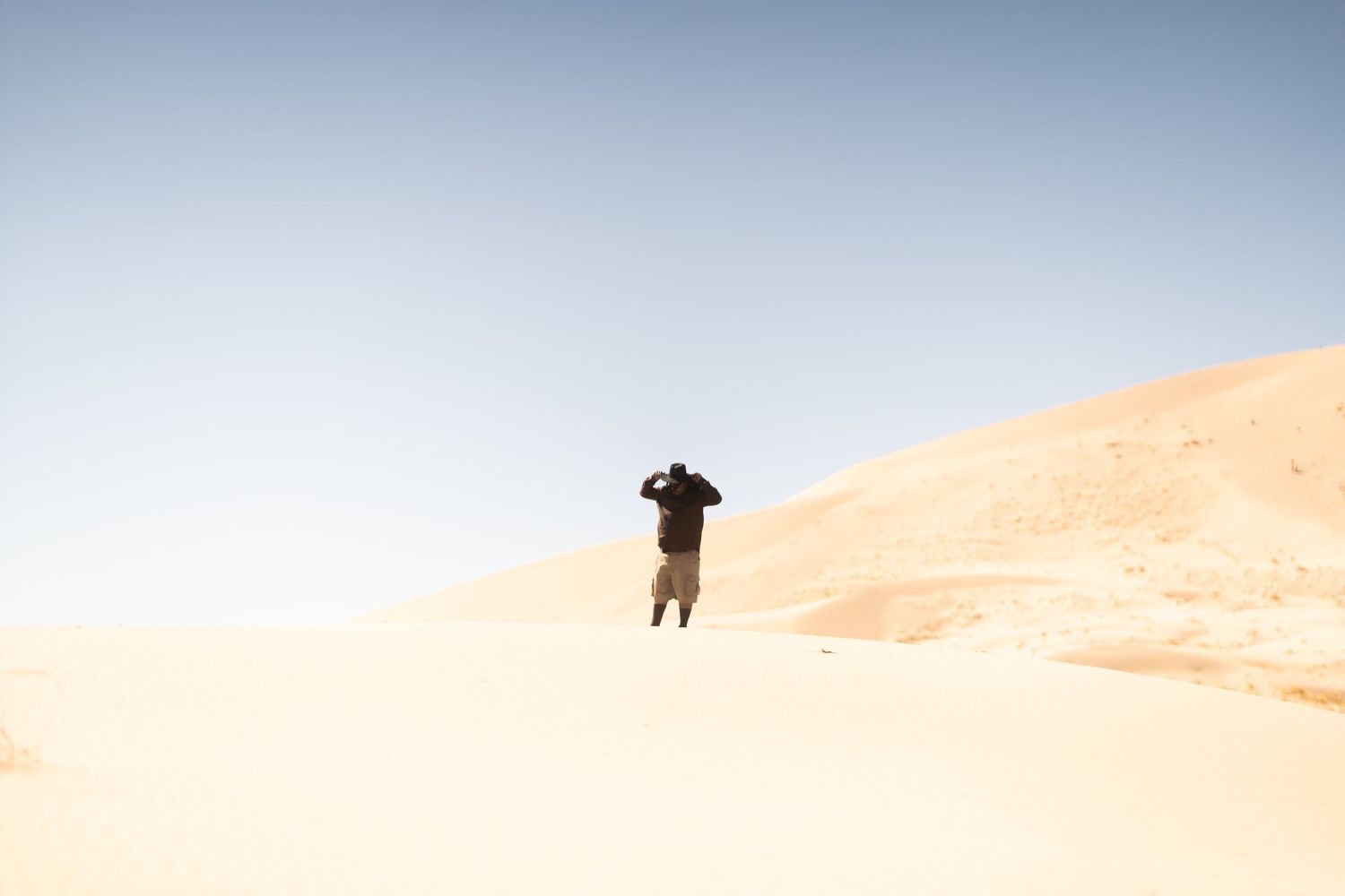 Person standing on a sand dune in a vast desert under clear blue sky.