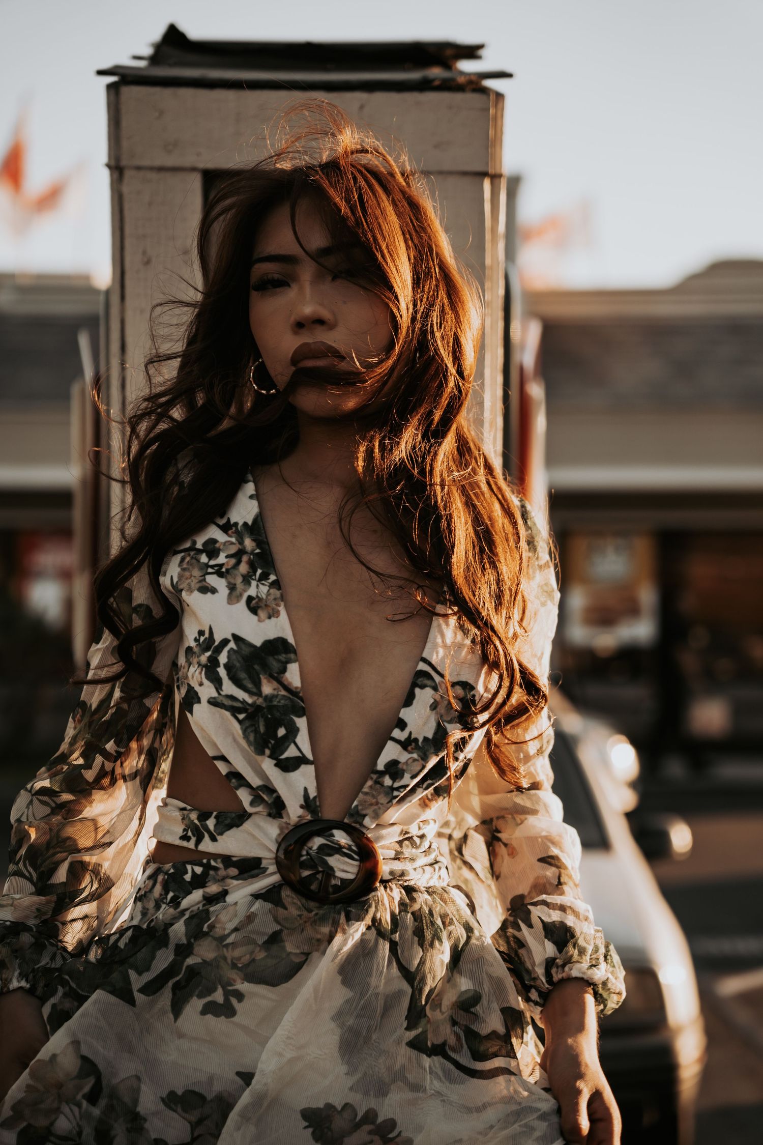 Woman with flowing auburn hair in floral deep-v dress posing outdoors in warm golden sunset light.