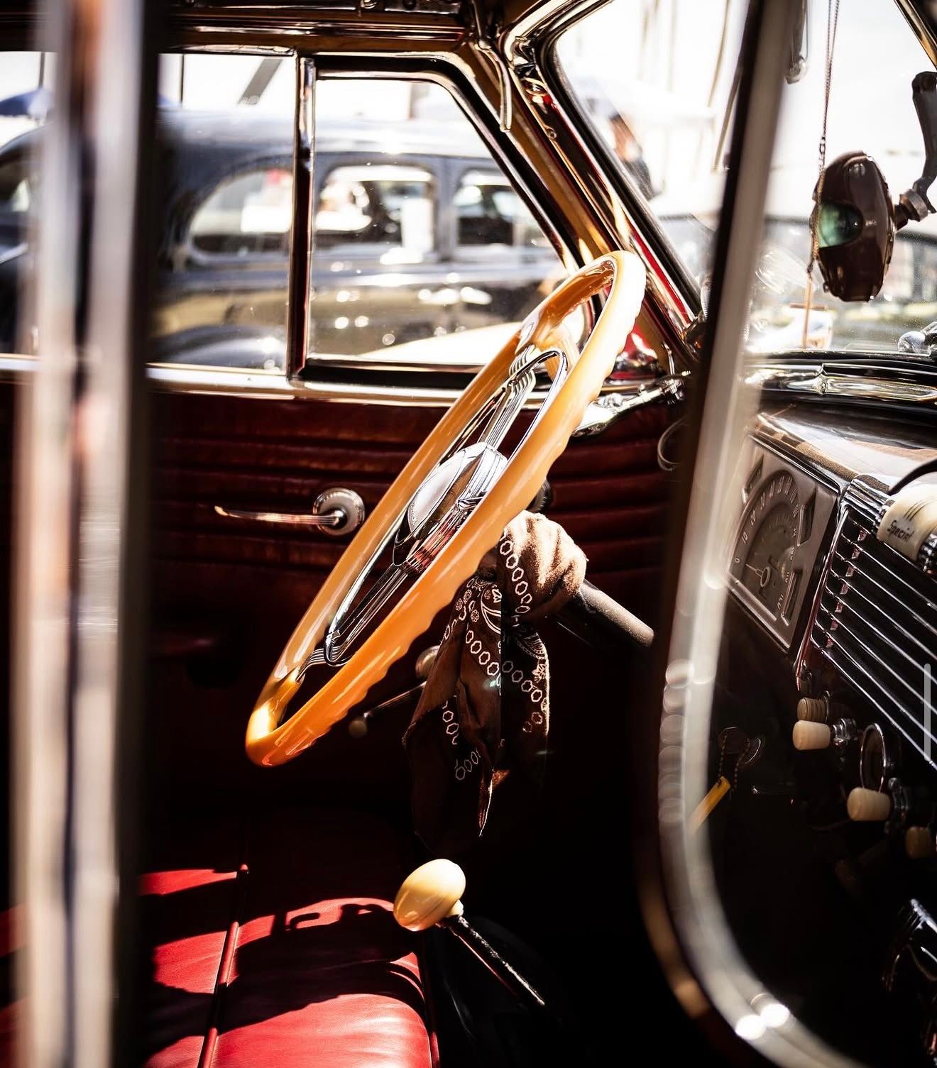 Vintage car interior with wooden steering wheel, red leather seats, and classic dashboard details.