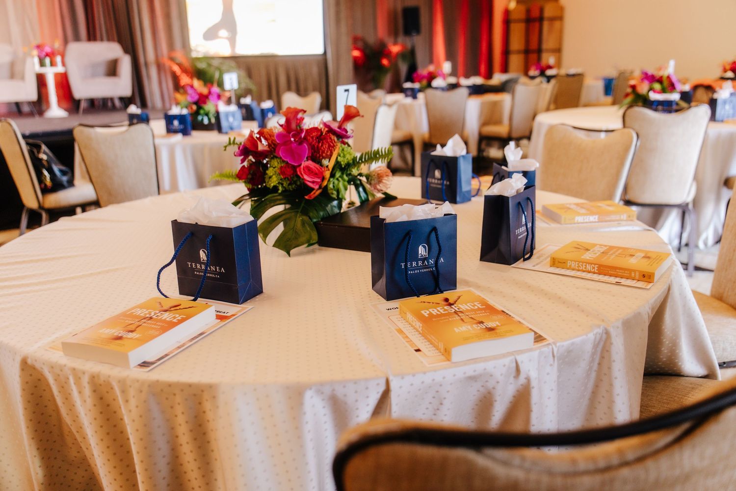 Elegant round banquet table with floral centerpiece, navy gift bags, and event programs for a formal dinner.