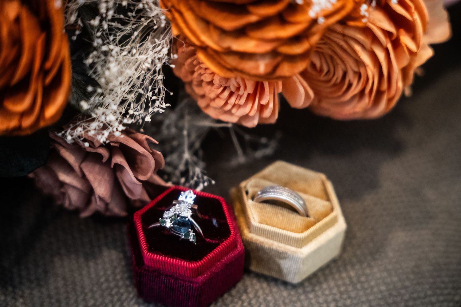 Diamond engagement ring and wedding band displayed in velvet boxes beside orange and mauve floral arrangement.