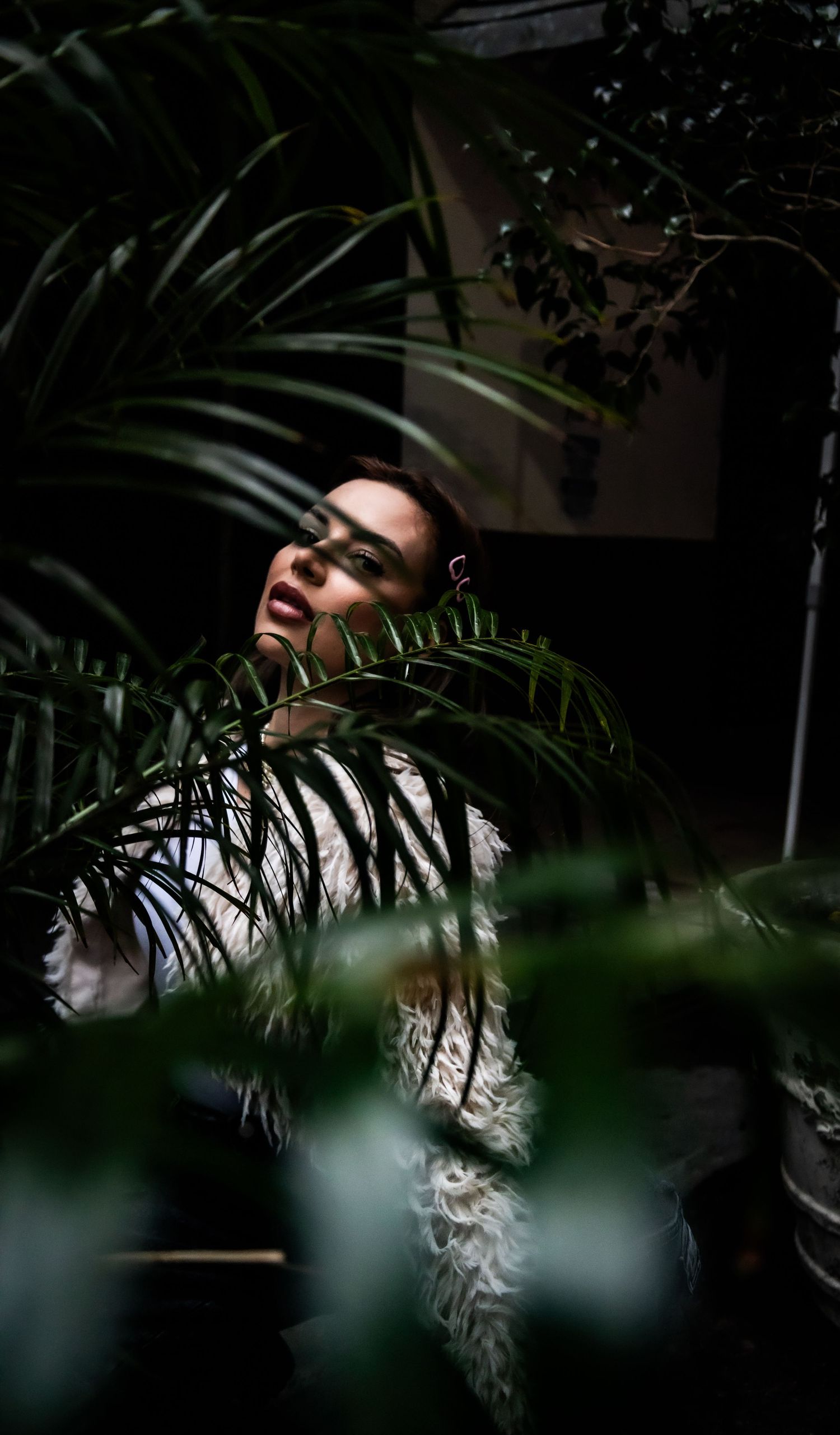 A woman gazing upward surrounded by lush tropical plants in dramatic moody lighting.