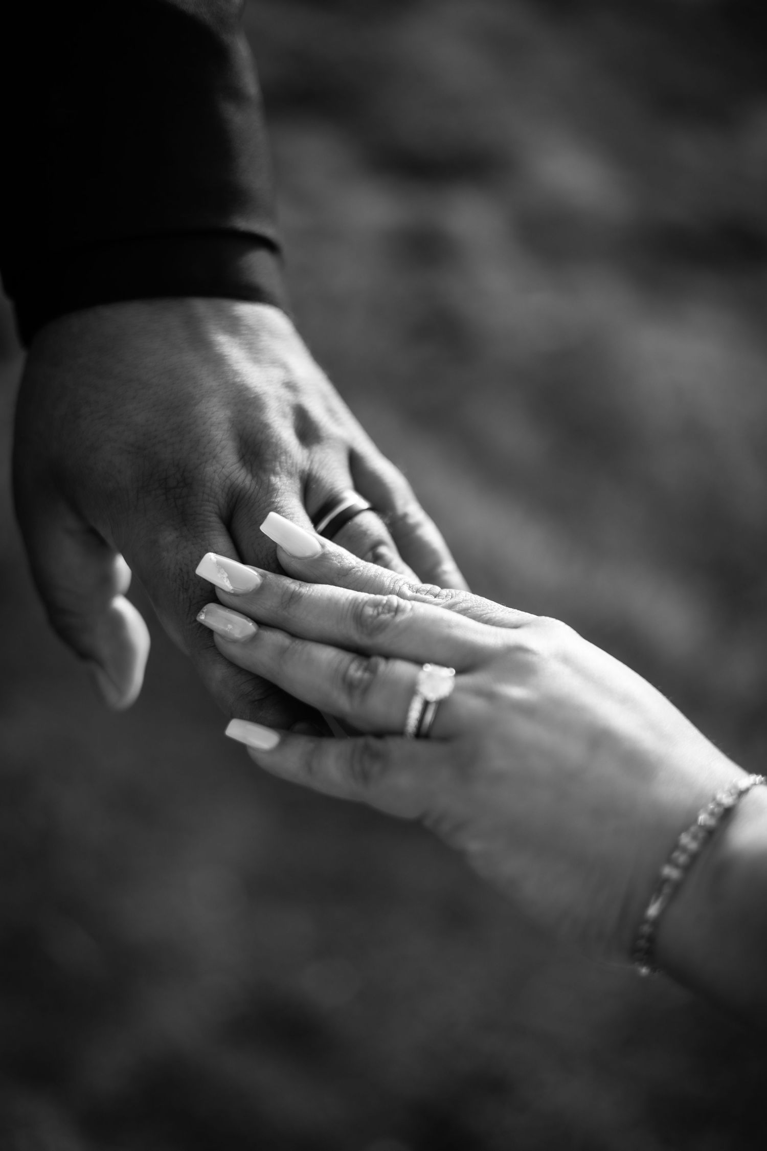 Black and white close-up of couple holding hands showing wedding rings and manicured nails with bracelet.