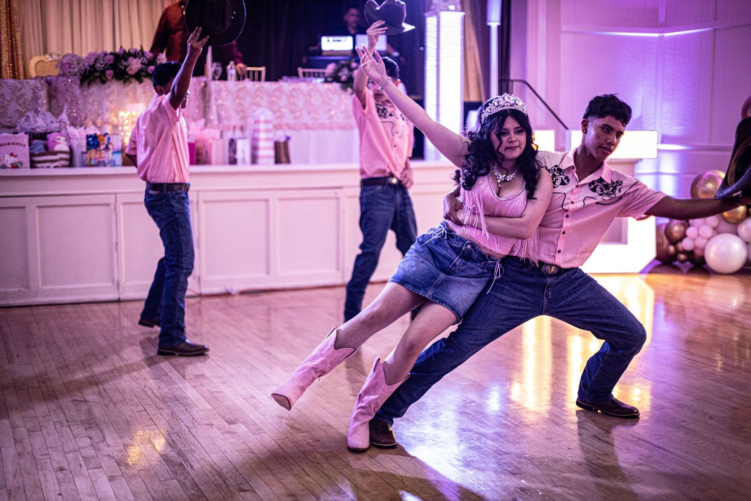 Quinceañera girl in pink outfit dances energetically with chambelán in decorated ballroom.