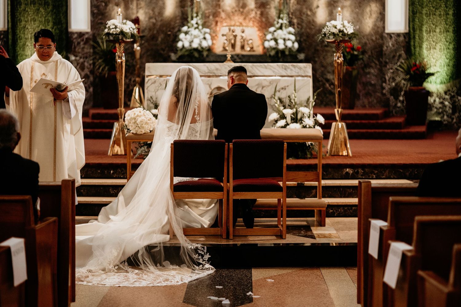 Bride and groom kneeling at the altar during a traditional Catholic church wedding ceremony with white floral decor.