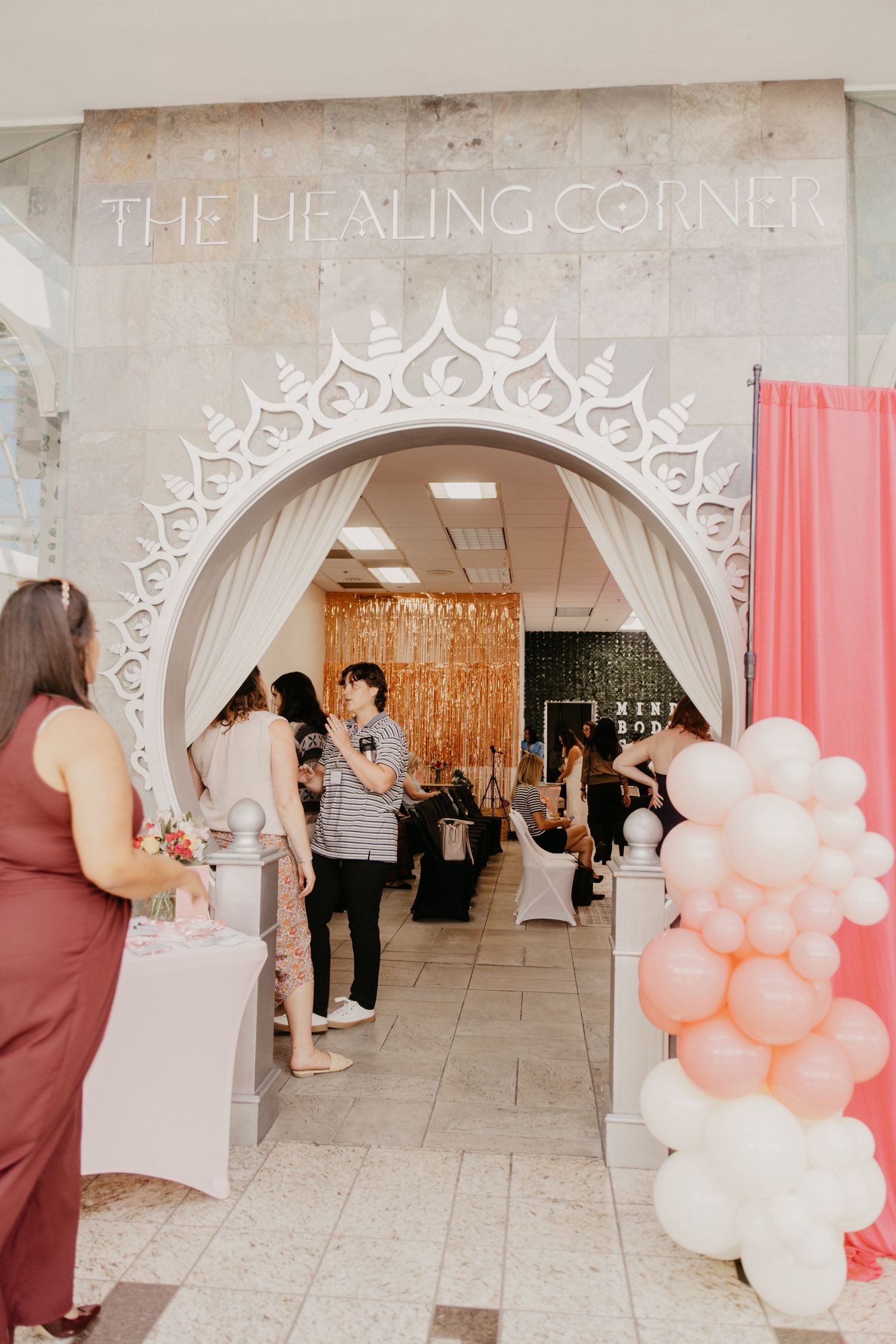 Elegant white arched entrance to The Healing Corner event space decorated with pink and white balloons.