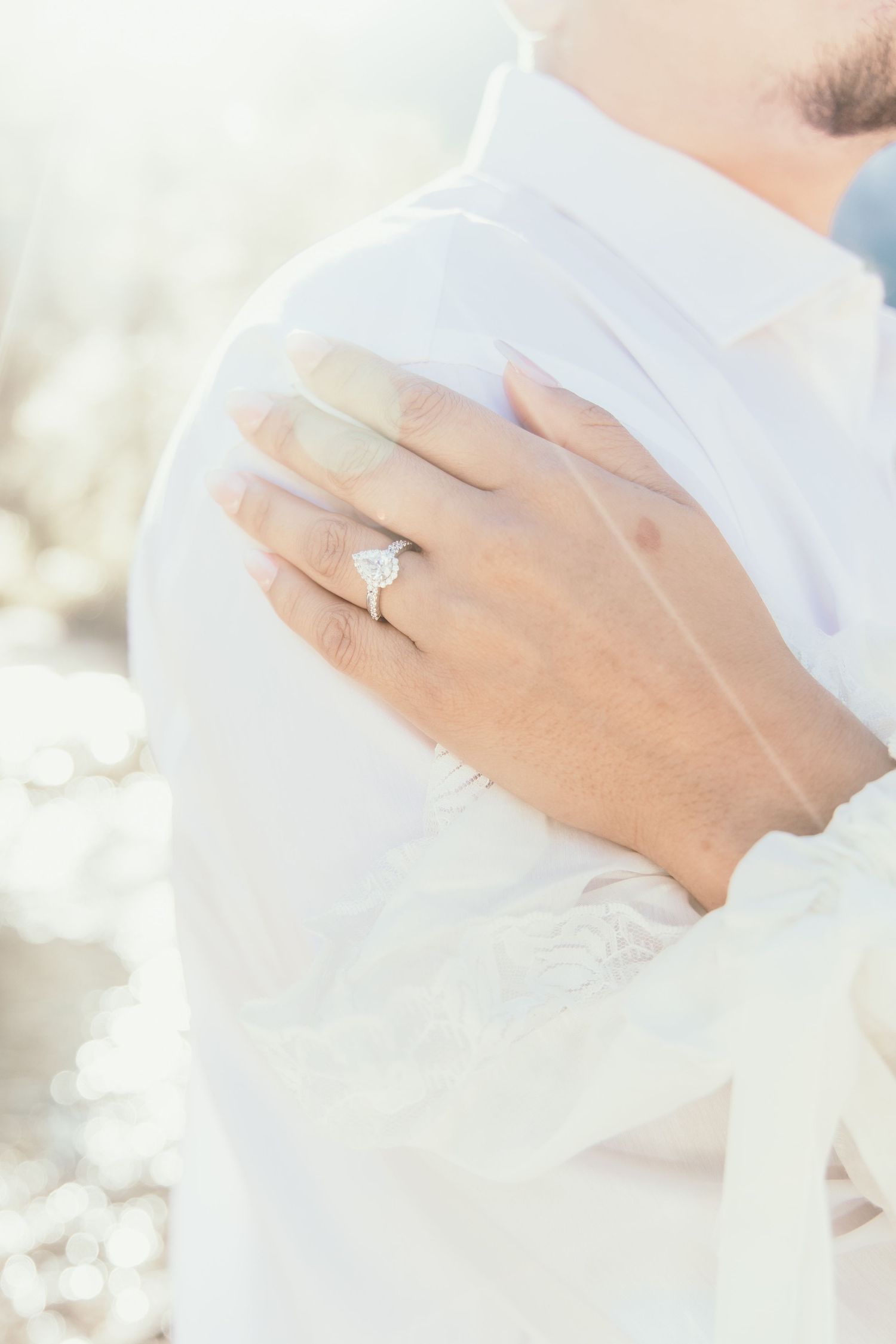 Close-up of a womans hand with a heart-shaped diamond engagement ring resting on a mans white dress shirt.