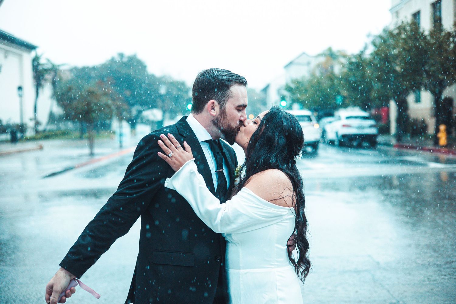 Bride and groom share passionate kiss in the rain on a city street.