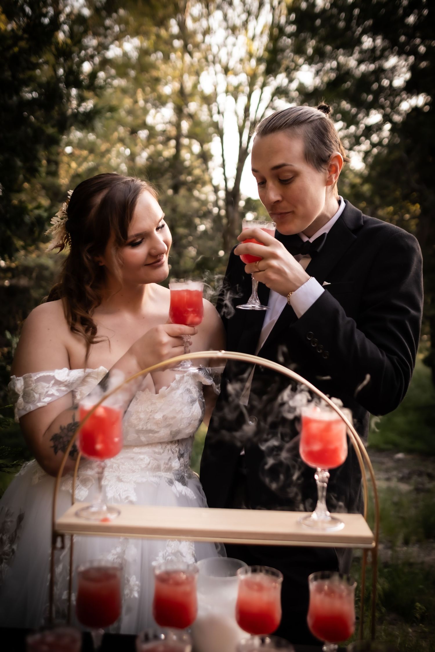 Bride and groom toasting with smoky red cocktails at an outdoor woodland wedding reception.