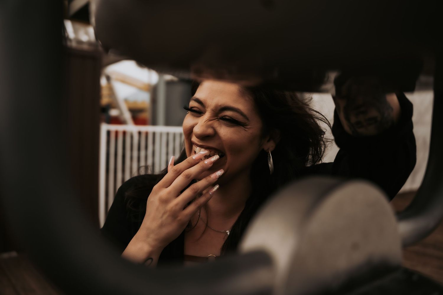 A woman laughing joyfully with her hand over her mouth in a dimly lit industrial setting.