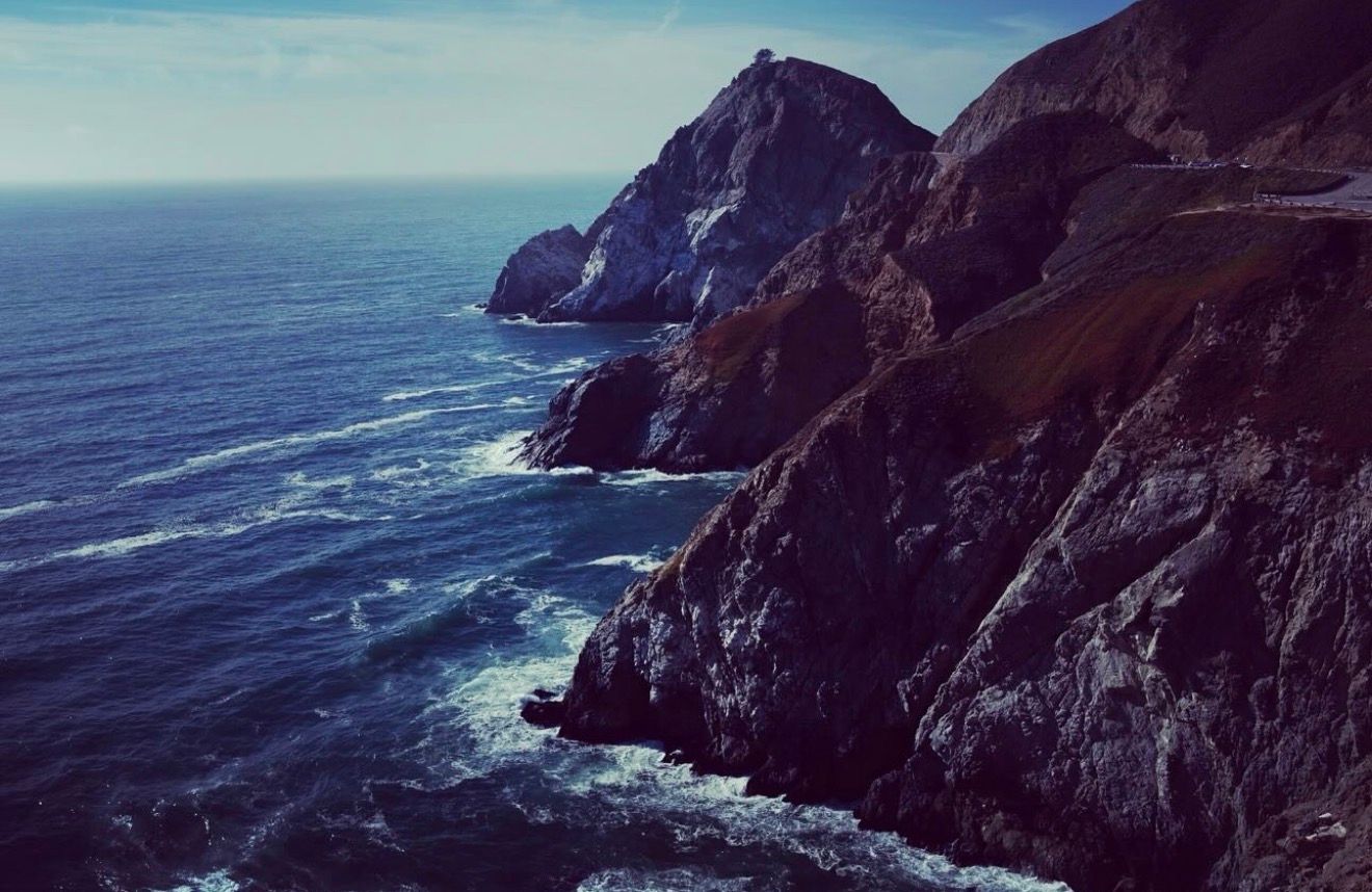Rocky coastal cliffs overlooking deep blue ocean waves with a lighthouse perched atop the rugged headland.
