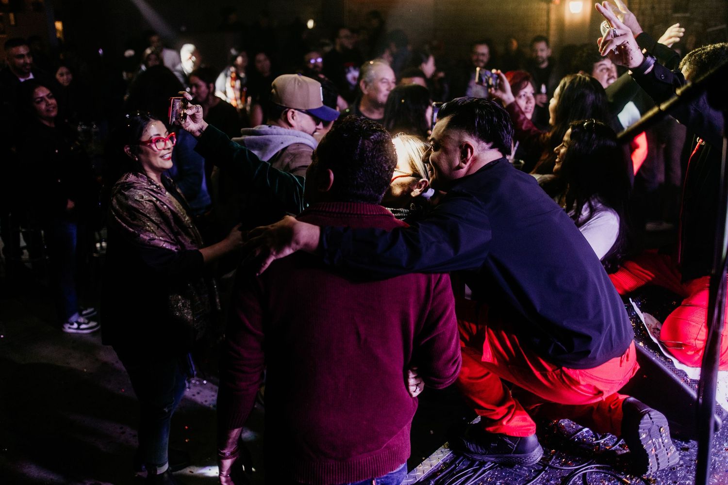 Energetic crowd interaction at night concert with performer crouching among fans in colorful attire.