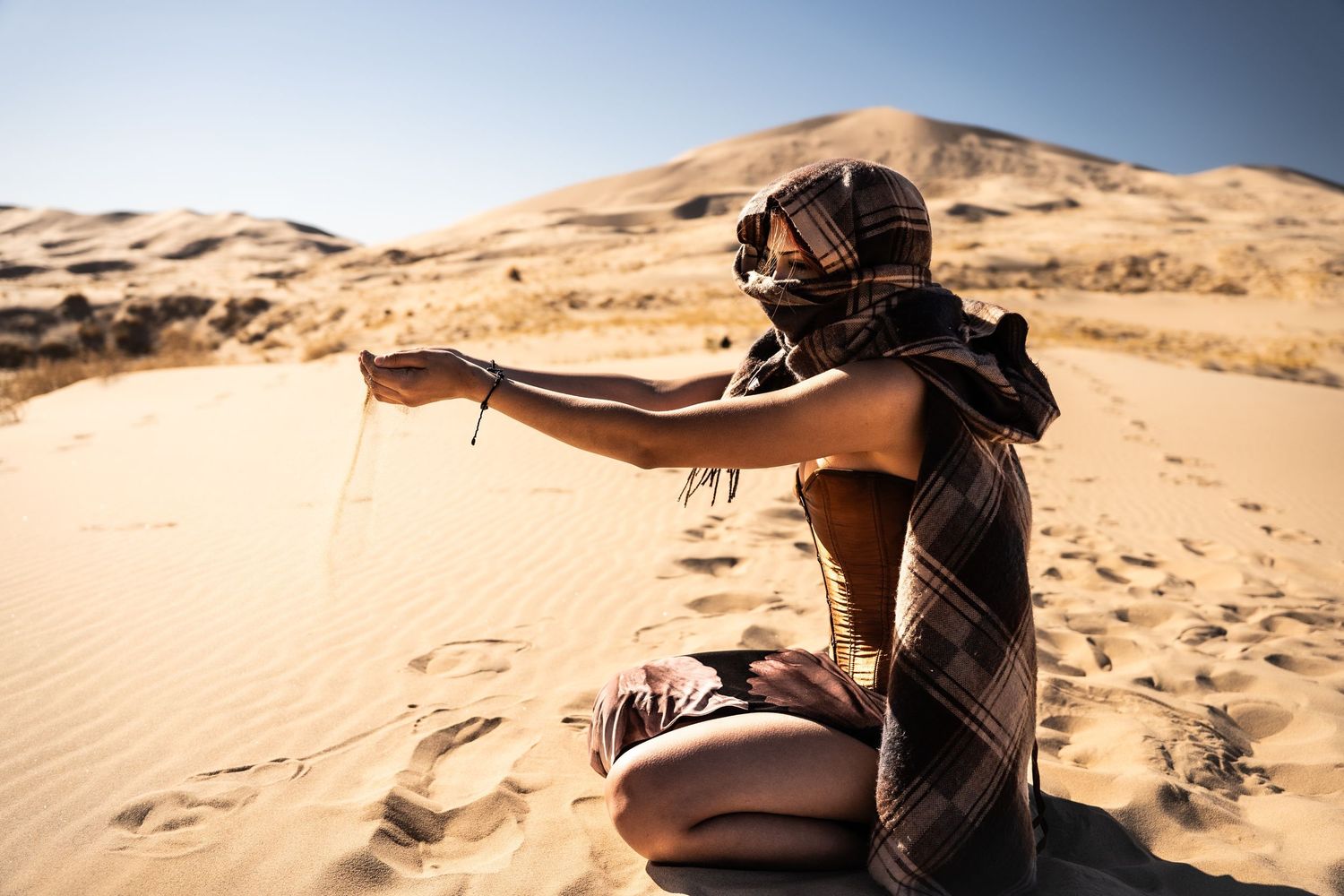 Woman in desert wrapping her head with a scarf while letting sand fall from her hand on a sunny day.