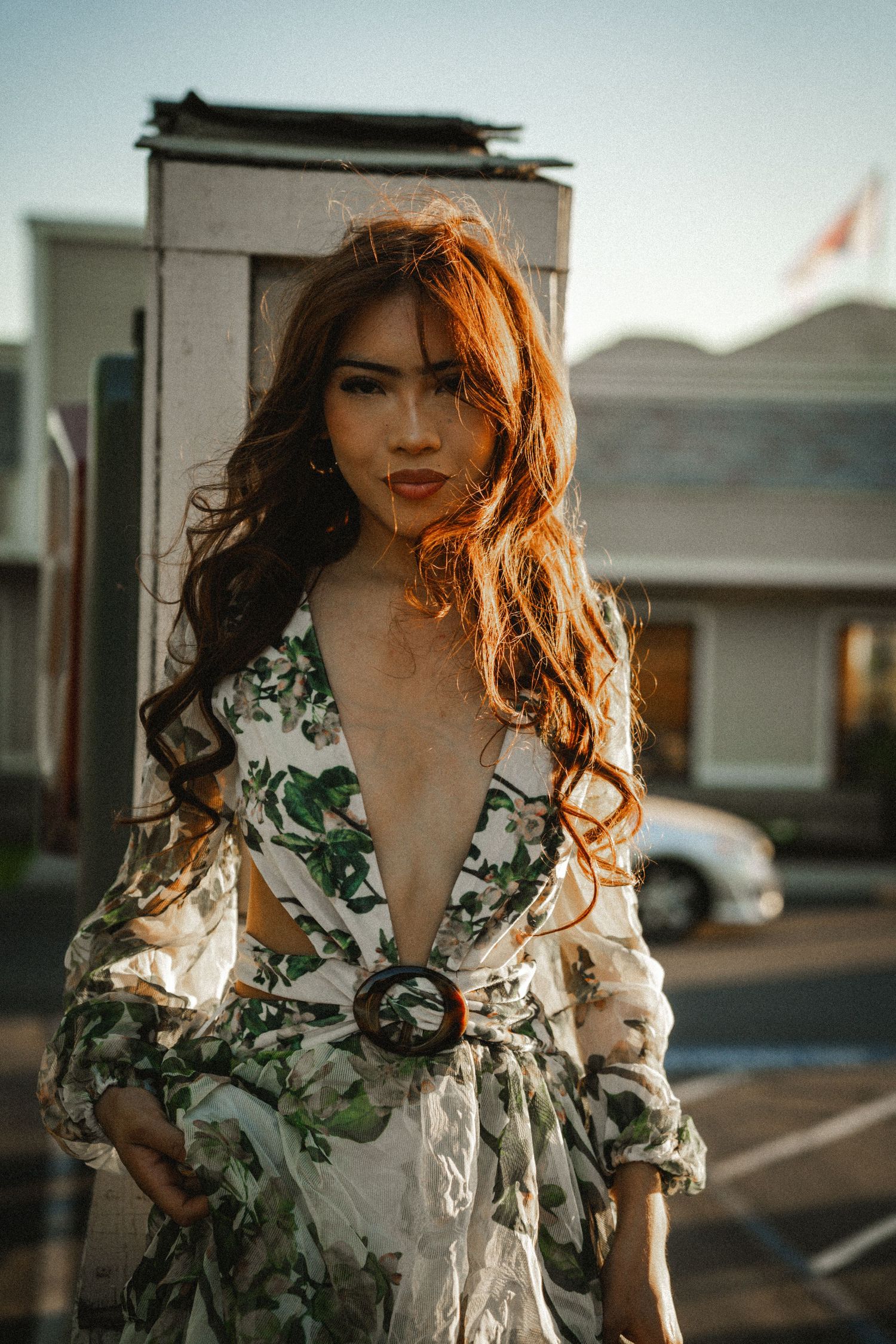 Woman with auburn hair in floral wrap dress posing outdoors at golden hour.