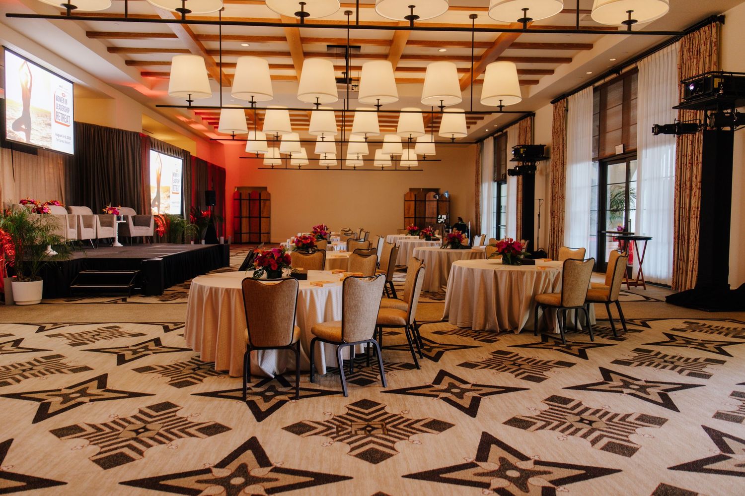 Elegant banquet hall with round tables, gold tablecloths, geometric patterned floor, and chandelier lighting for a formal event.
