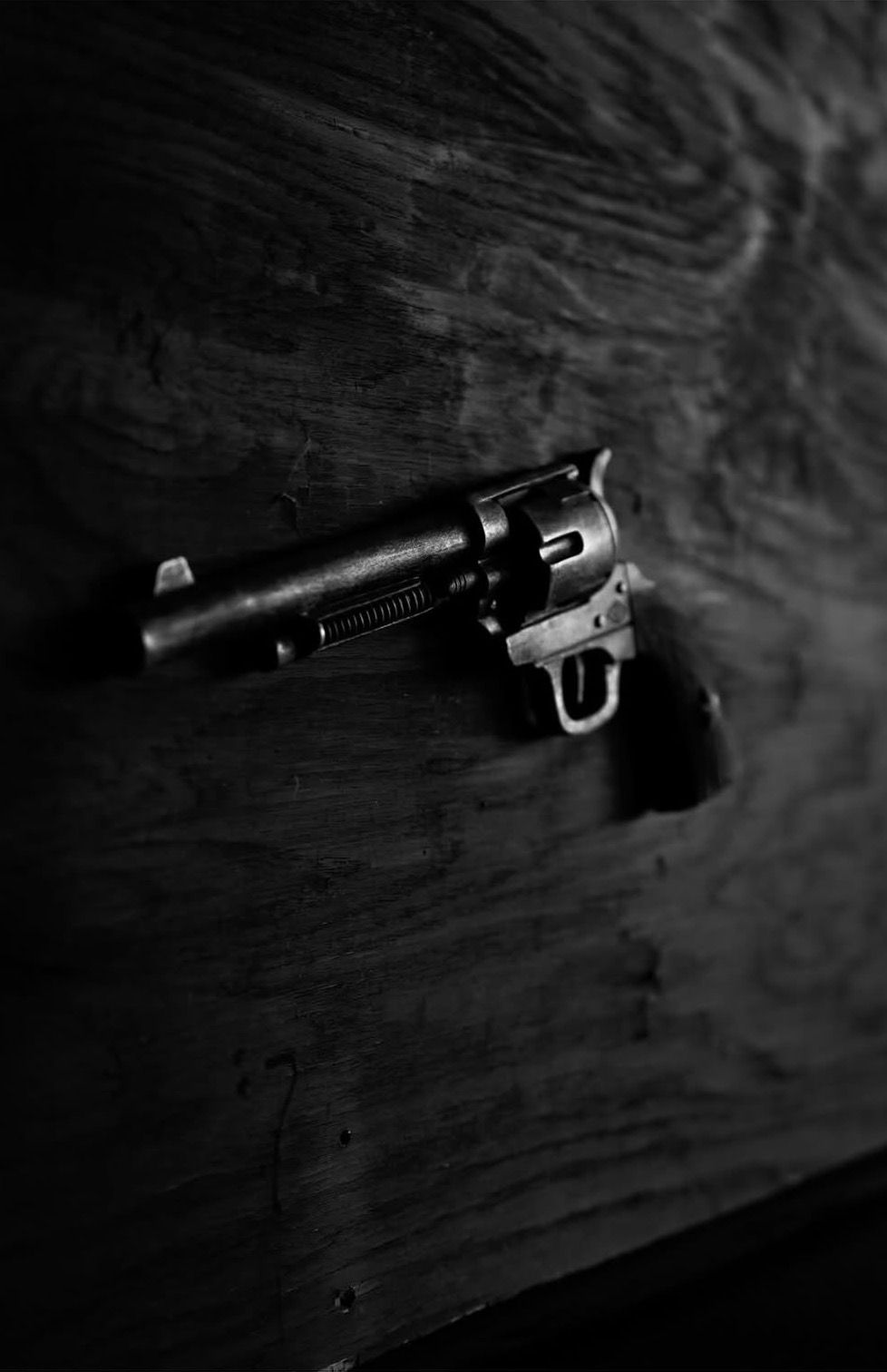 Black and white photo of a vintage revolver pistol resting on a dark wooden surface.