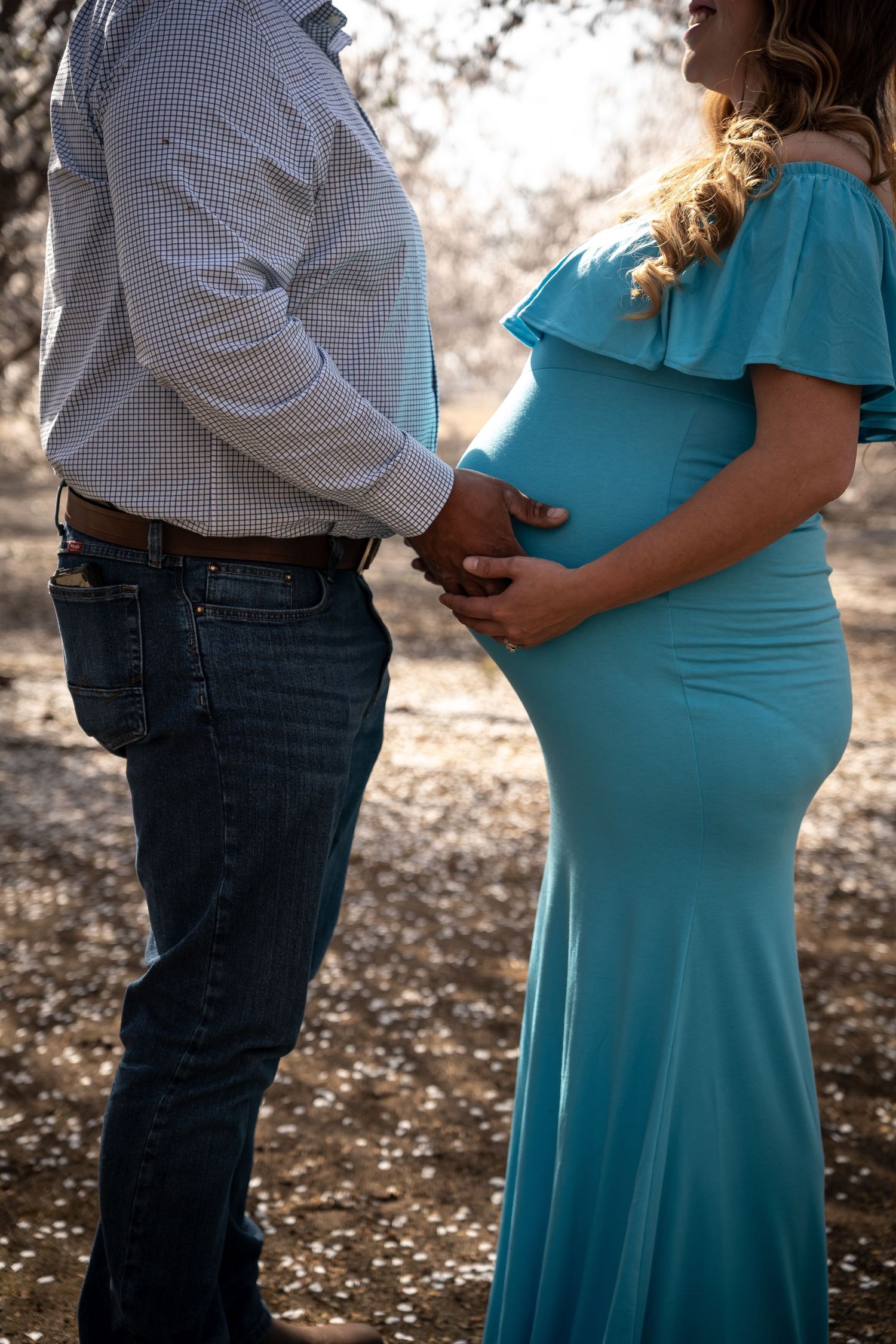 A couple holds hands tenderly as the pregnant woman in a teal gown cradles her baby bump.