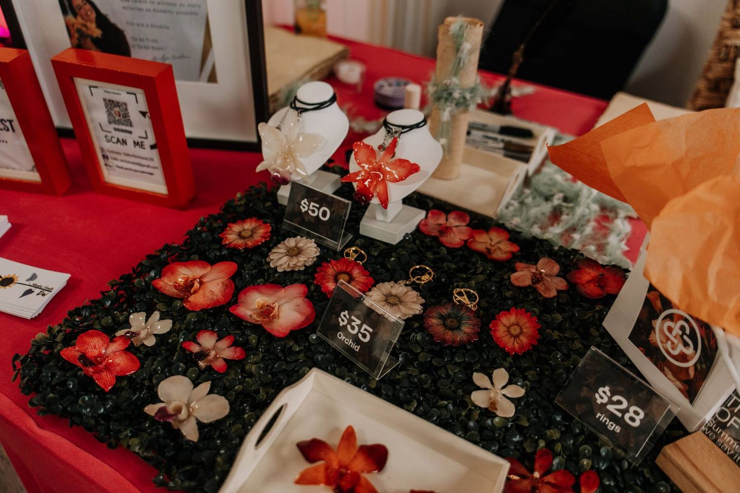 A vendor table displays handmade floral resin jewelry with price tags.