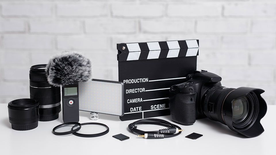 A filmmaking equipment flat lay featuring a DSLR camera, clapperboard, lenses, and microphone.