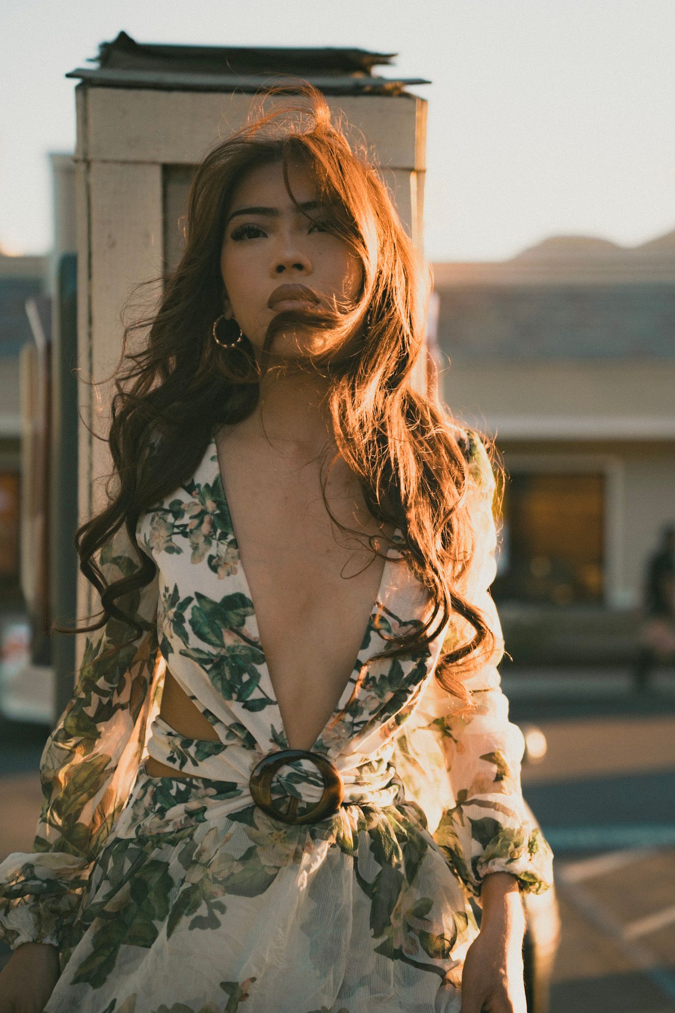 Young woman in floral dress with deep V-neckline posing at sunset.