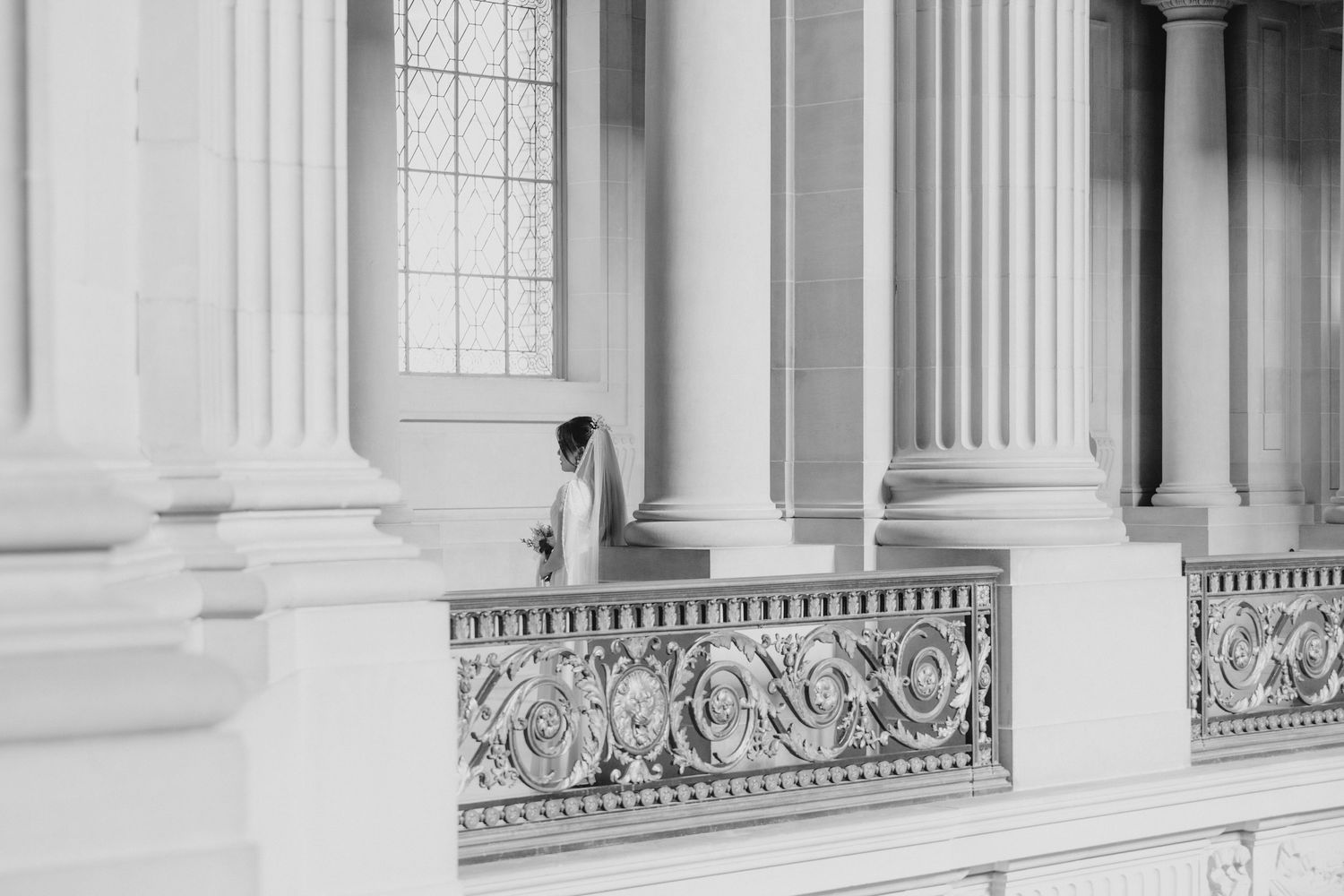 Black and white photo of bride in wedding gown standing among grand classical columns.