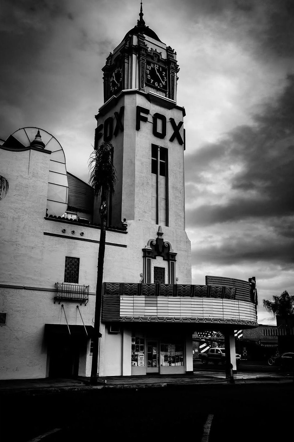 Black and white photo of the historic Fox Theatre building with clock tower and marquee under dramatic cloudy skies.