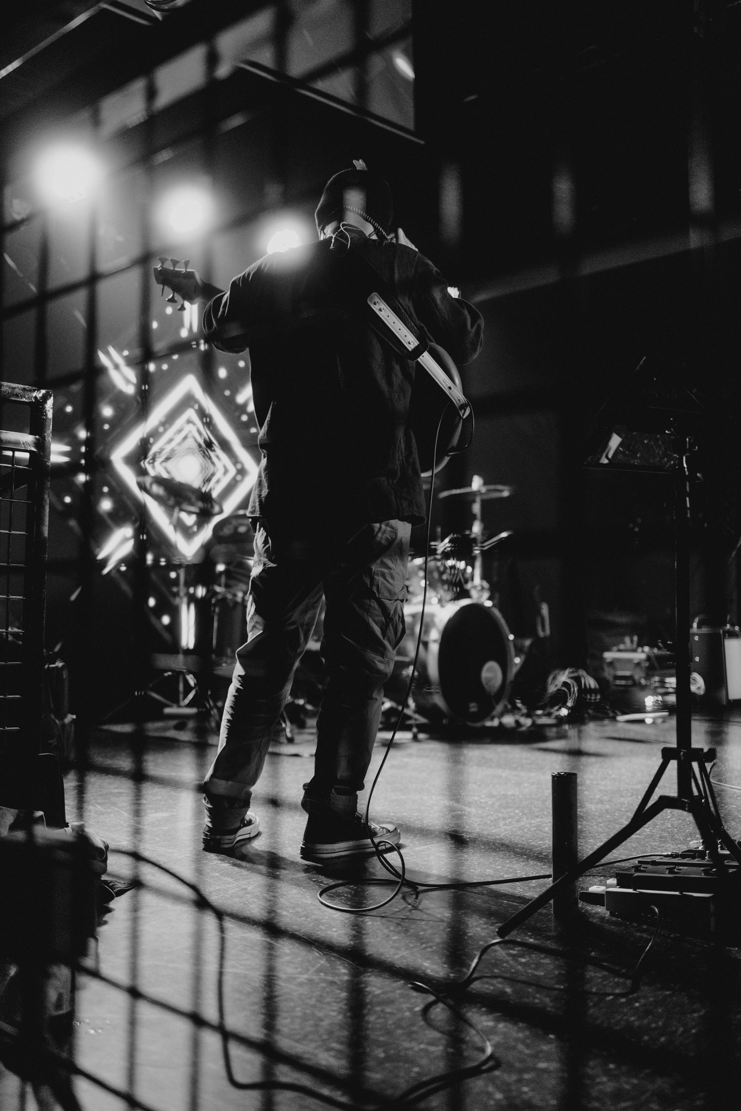 Black and white silhouette of a performer on stage with a diamond neon light and drum kit in background.