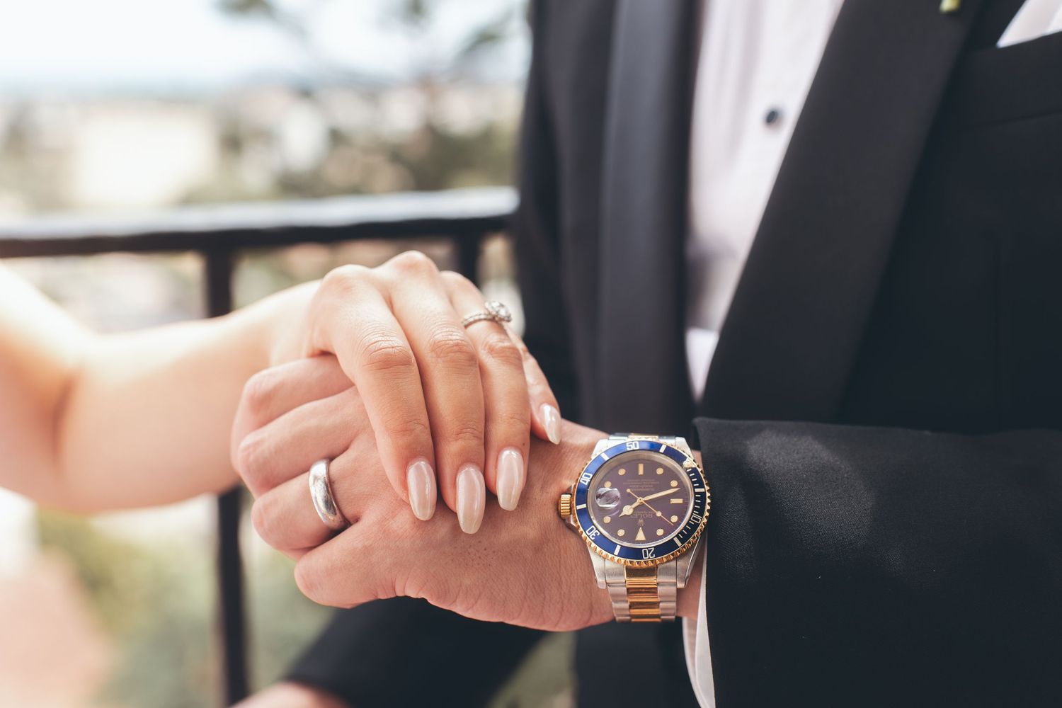 Couple holding hands at wedding, bride with manicured nails and groom wearing a gold Rolex Submariner watch.