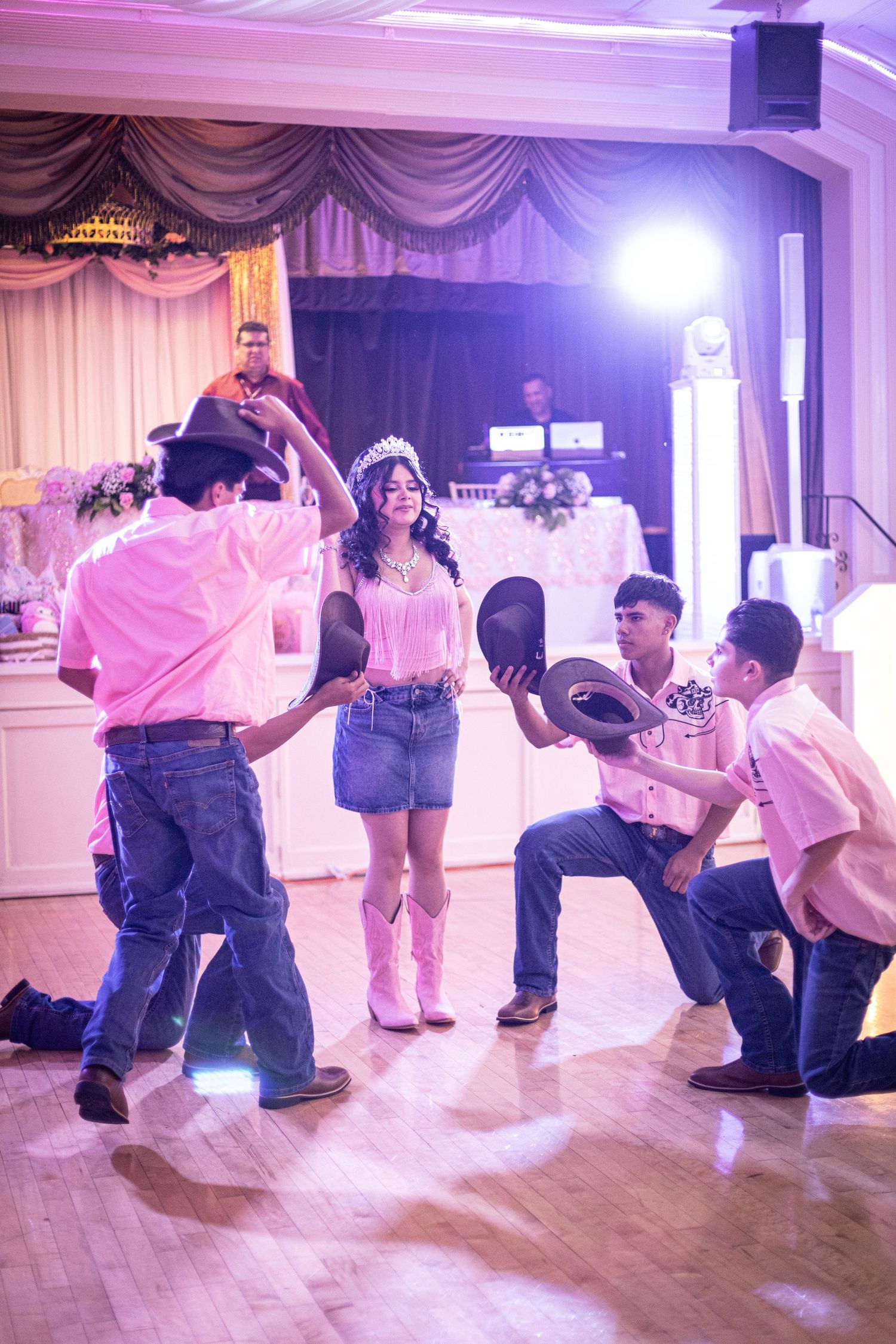 Young woman in crown and pink outfit dances with chambelanes in cowboy hats at a quinceañera celebration.