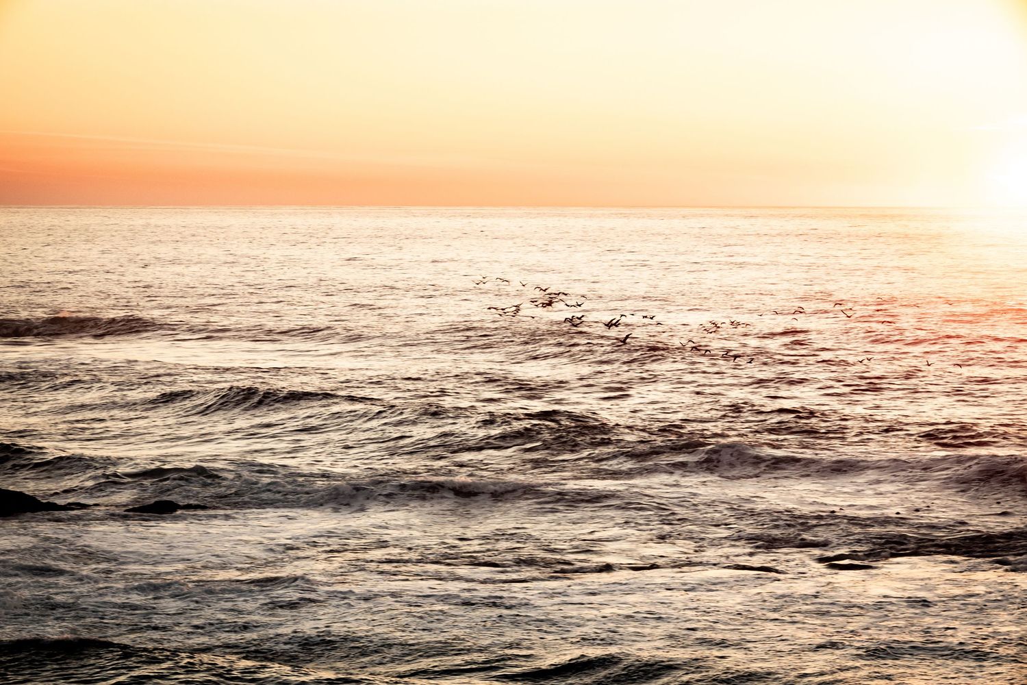 Golden sunset over ocean waves with warm orange sky reflecting on choppy sea surface.