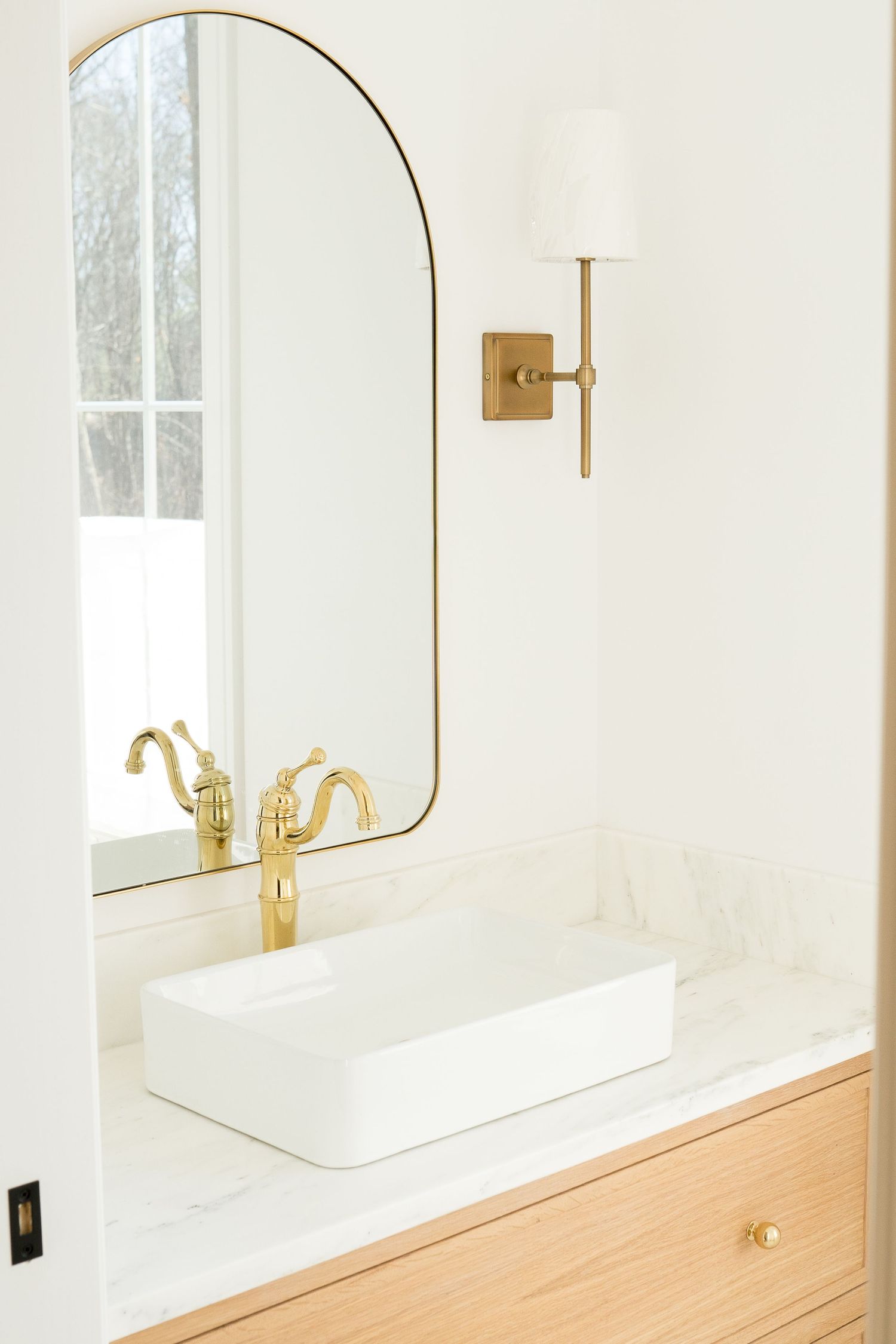 Minimalist bathroom design featuring round mirrors with brass accents and wooden cabinetry.
