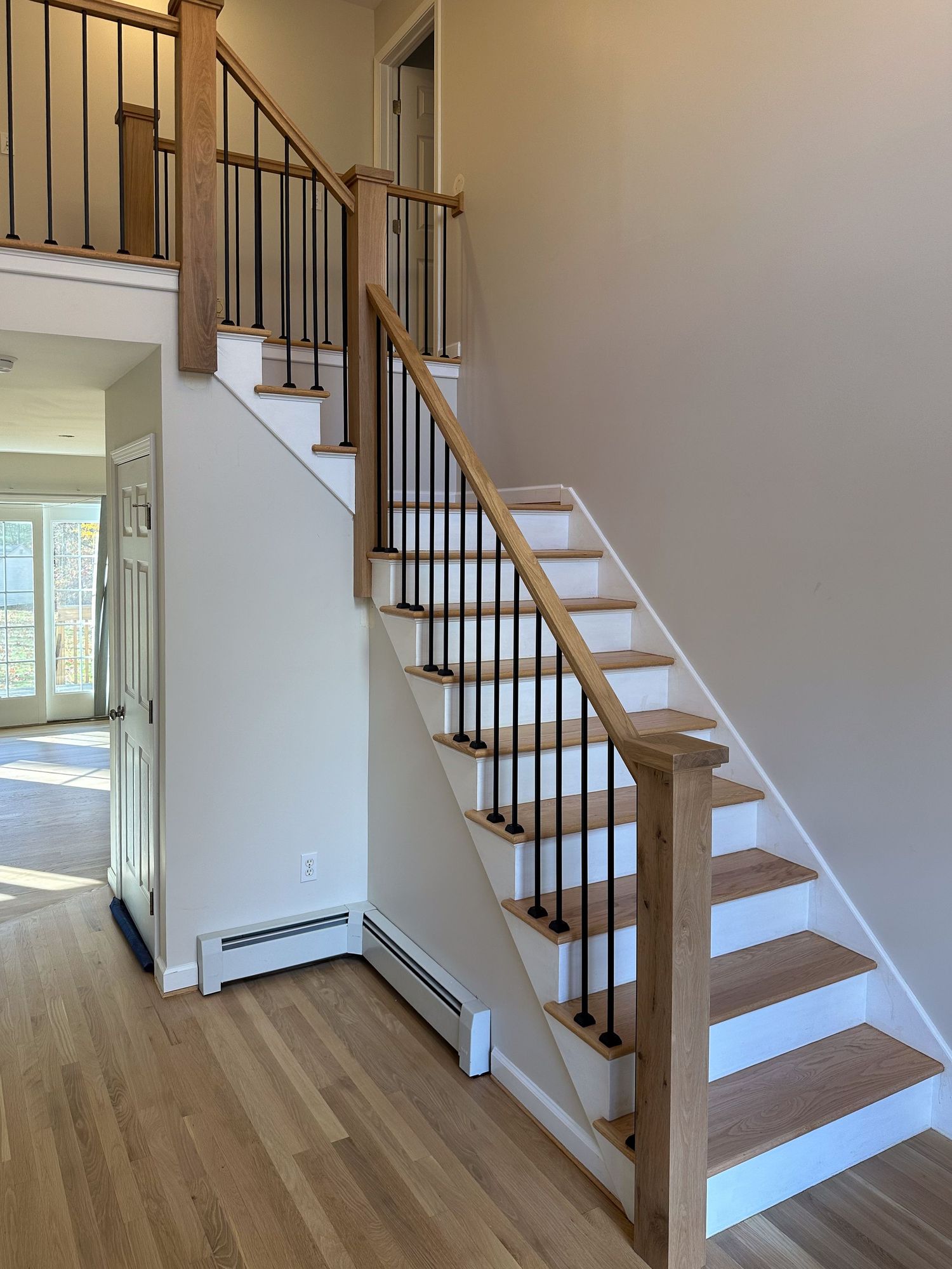 Modern staircase featuring white treads and metal balusters with wooden handrail.