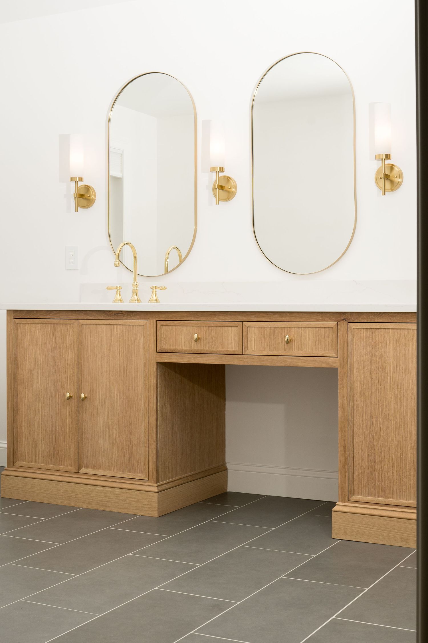 Sleek bathroom vanity installation with round mirrors, brass fixtures, and gray tile flooring.