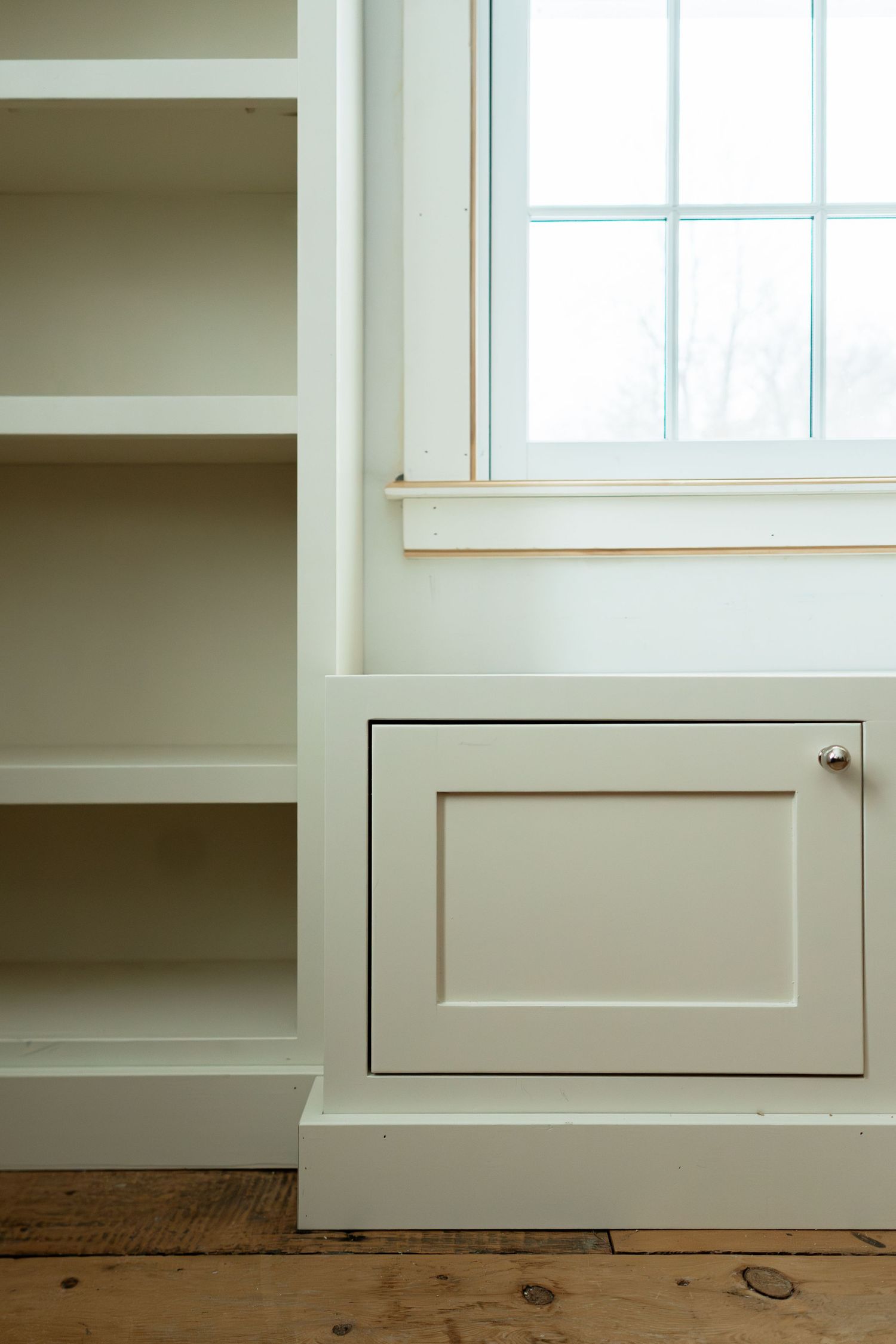 Low angle view of white built-in cabinets and shelving with rustic wood flooring.