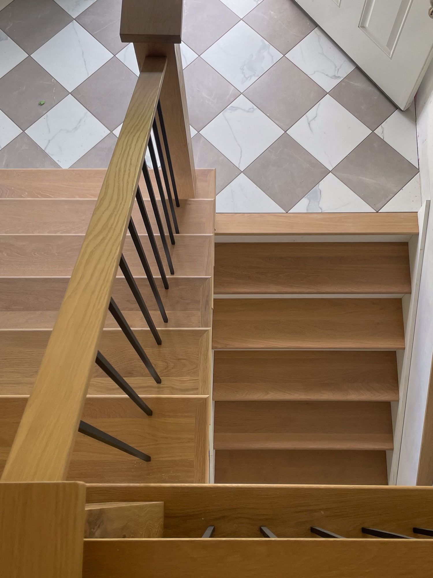 Wooden staircase with black metal balusters and checkerboard pattern floor tiles.