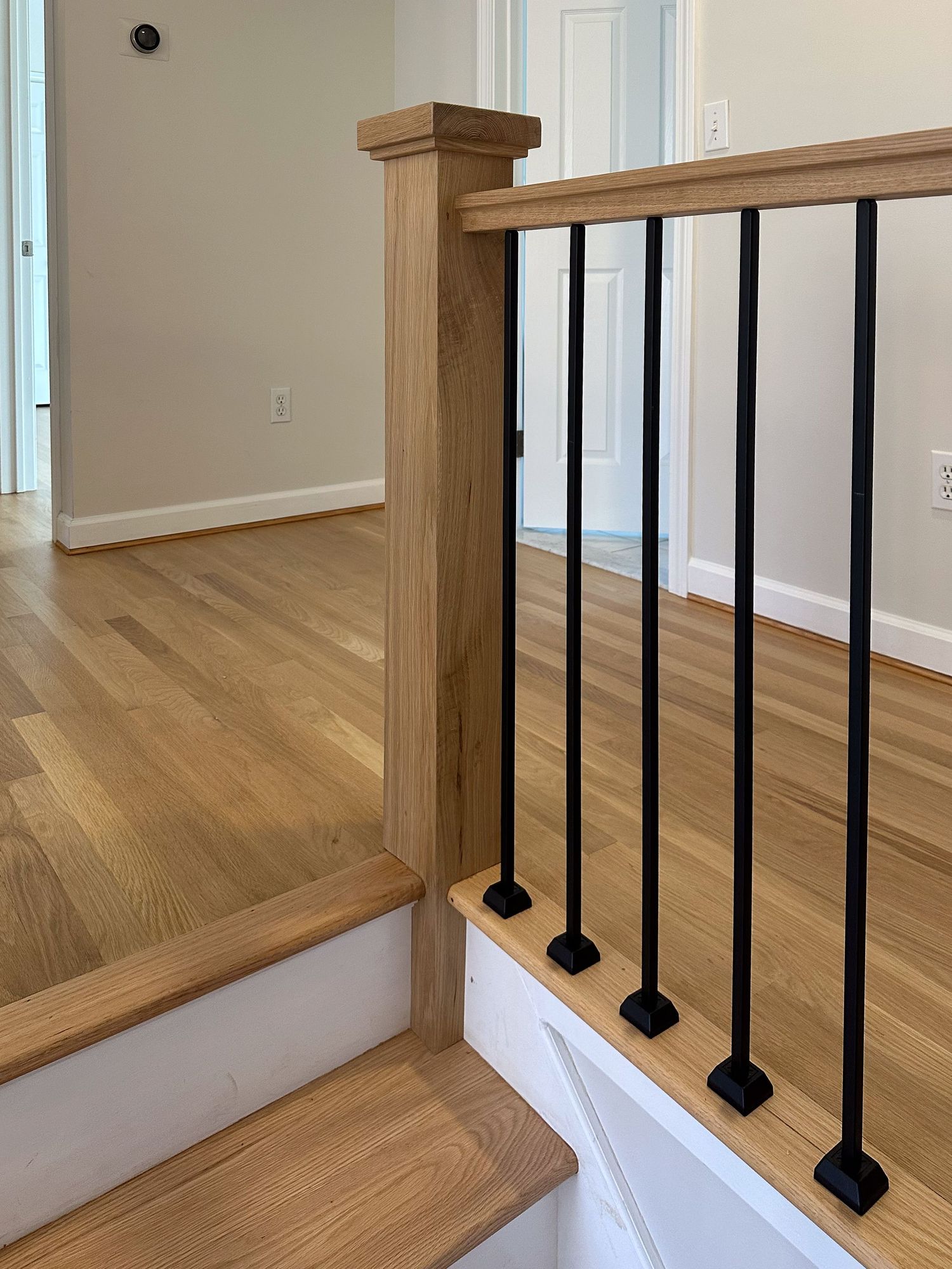 Close-up view of wooden stair treads with black metal balusters and wooden handrail detail.