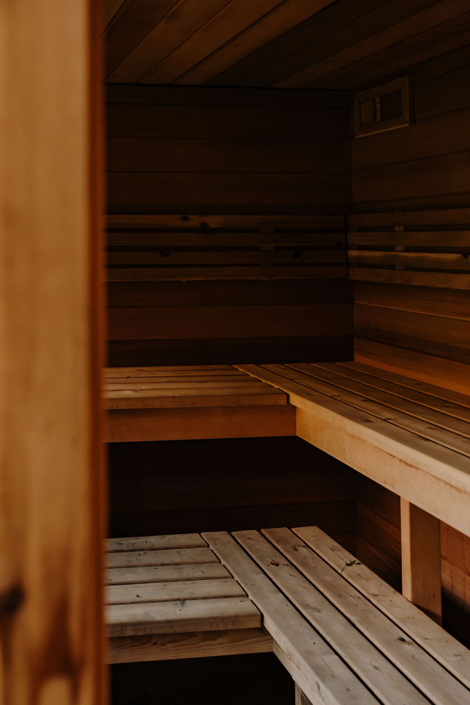 Empty wooden sauna interior with tiered cedar benches, warm lighting and a small vent, ideal for relaxation and wellness.