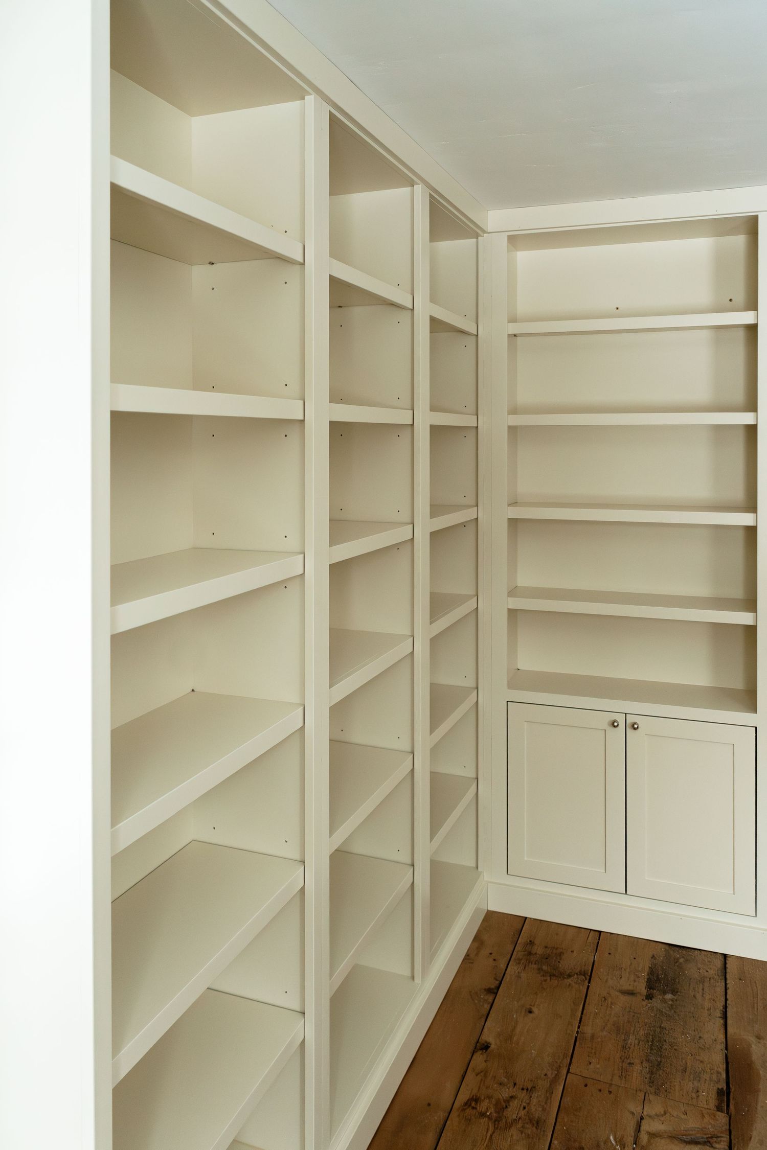 Corner view of empty white built-in shelving system with adjustable shelves and lower cabinets.