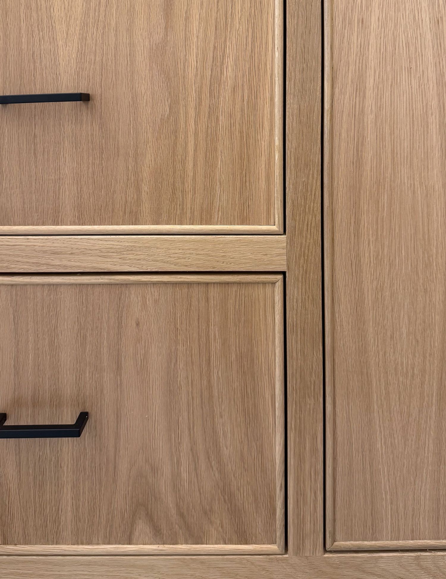 Close-up of modern light wood cabinet drawers with black handles showing clean lines and grain detail.