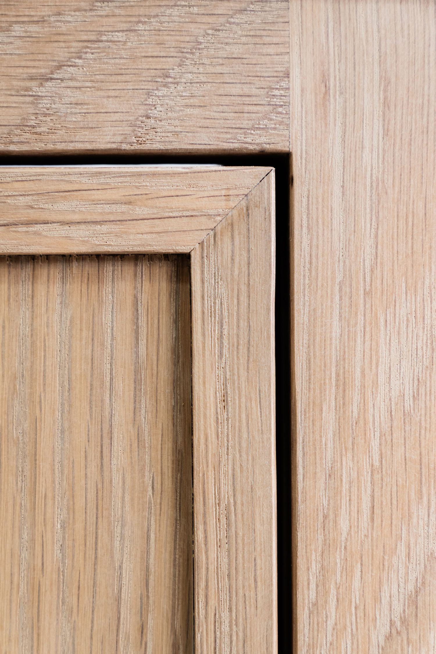 Close-up of a light oak wood cabinet door panel showing natural grain texture and mitered frame joinery.