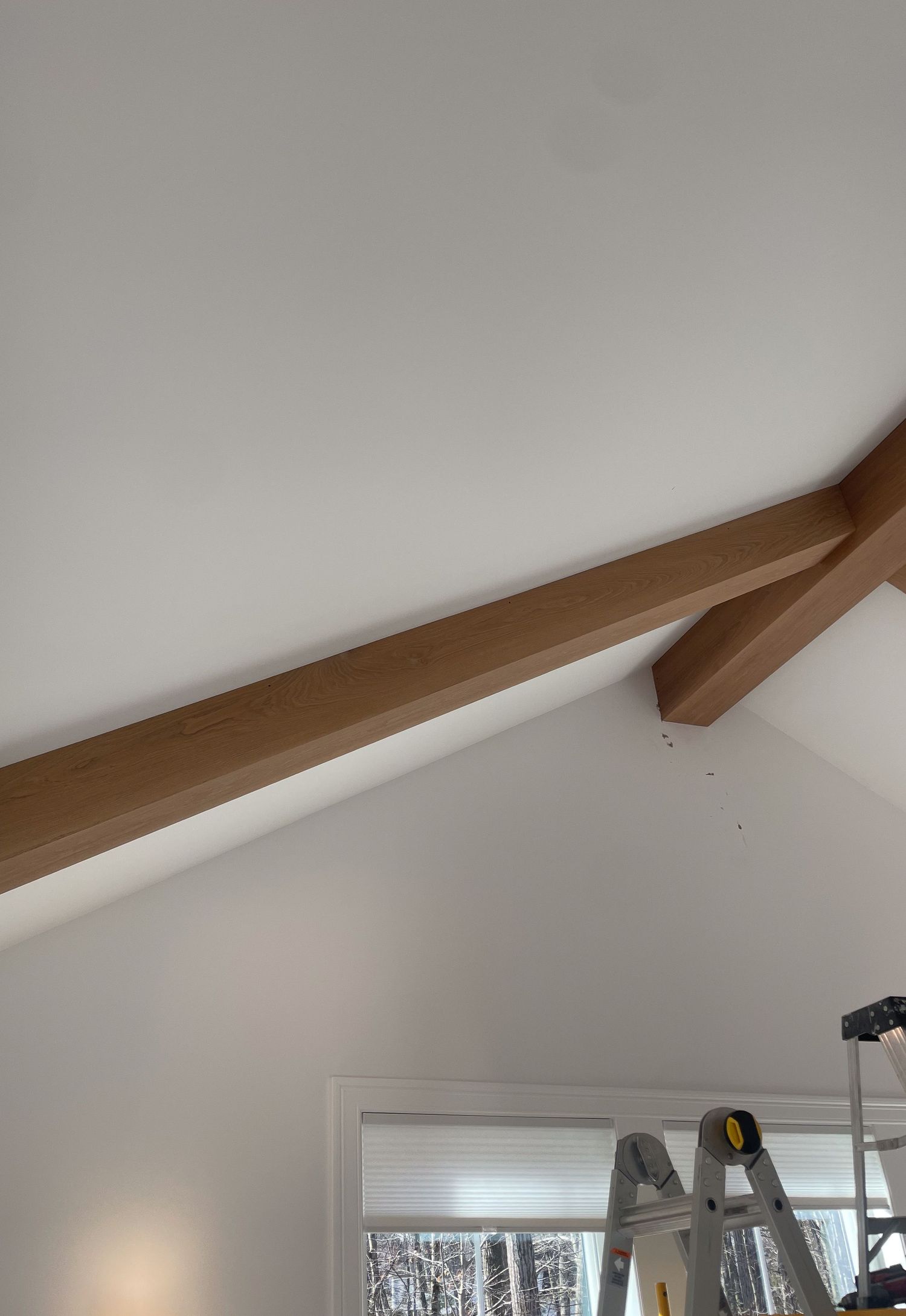 Exposed wooden beams line a white vaulted ceiling in a modern interior renovation.