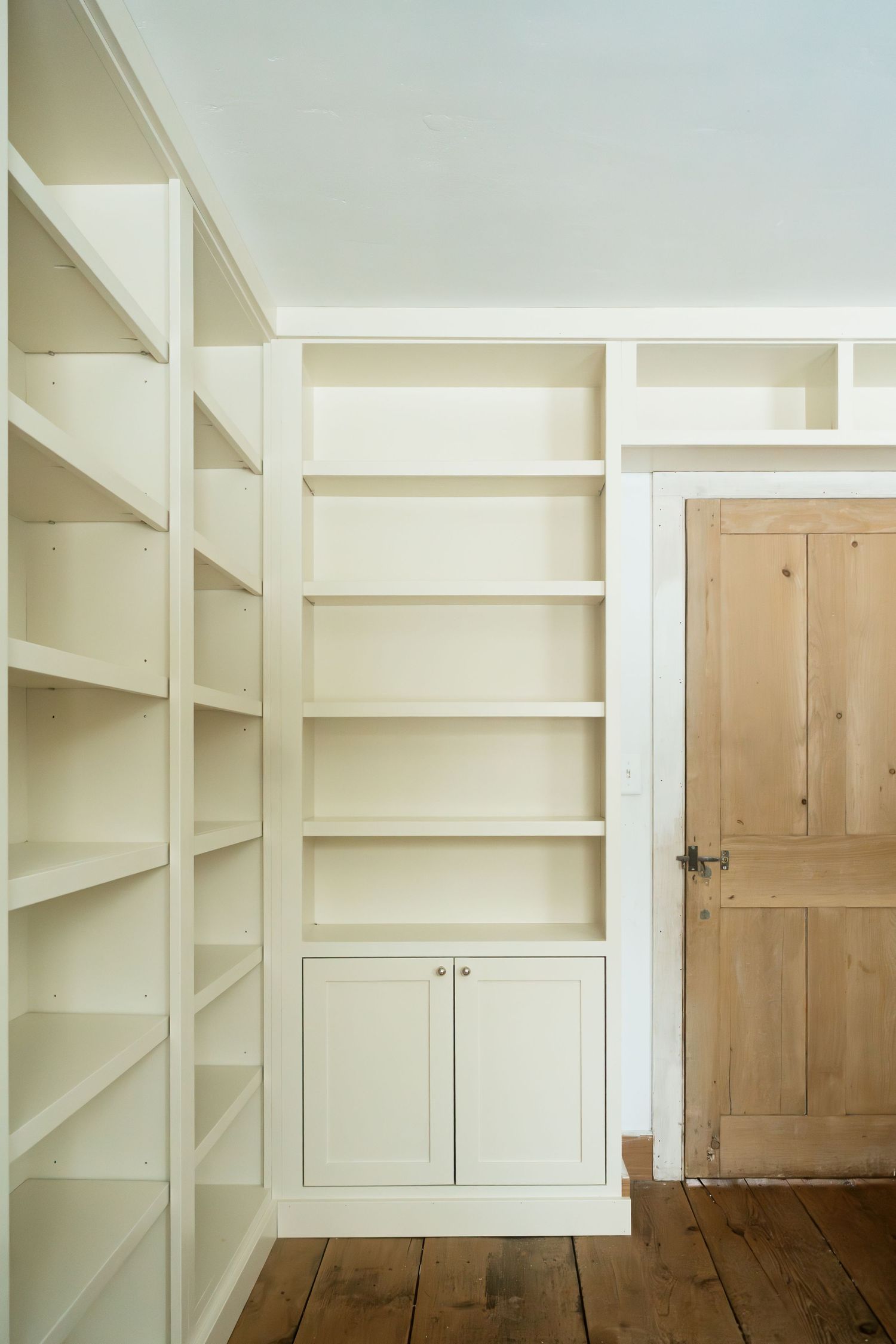 Floor-to-ceiling white built-in shelving with cabinets and a wooden door against white walls.