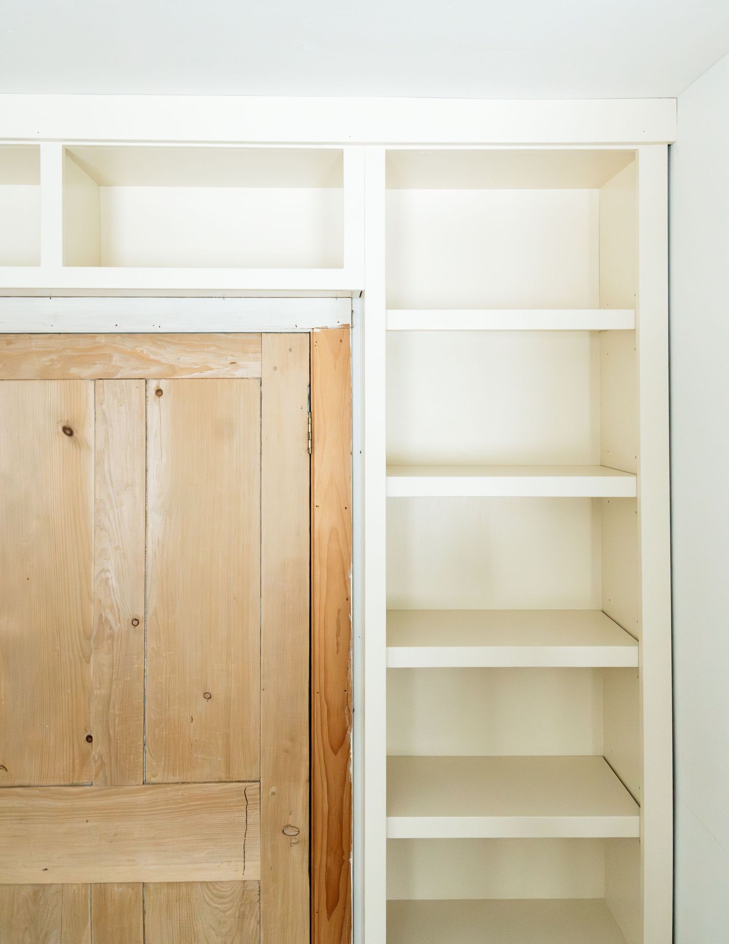 White built-in shelving unit next to natural wood door in rustic interior.