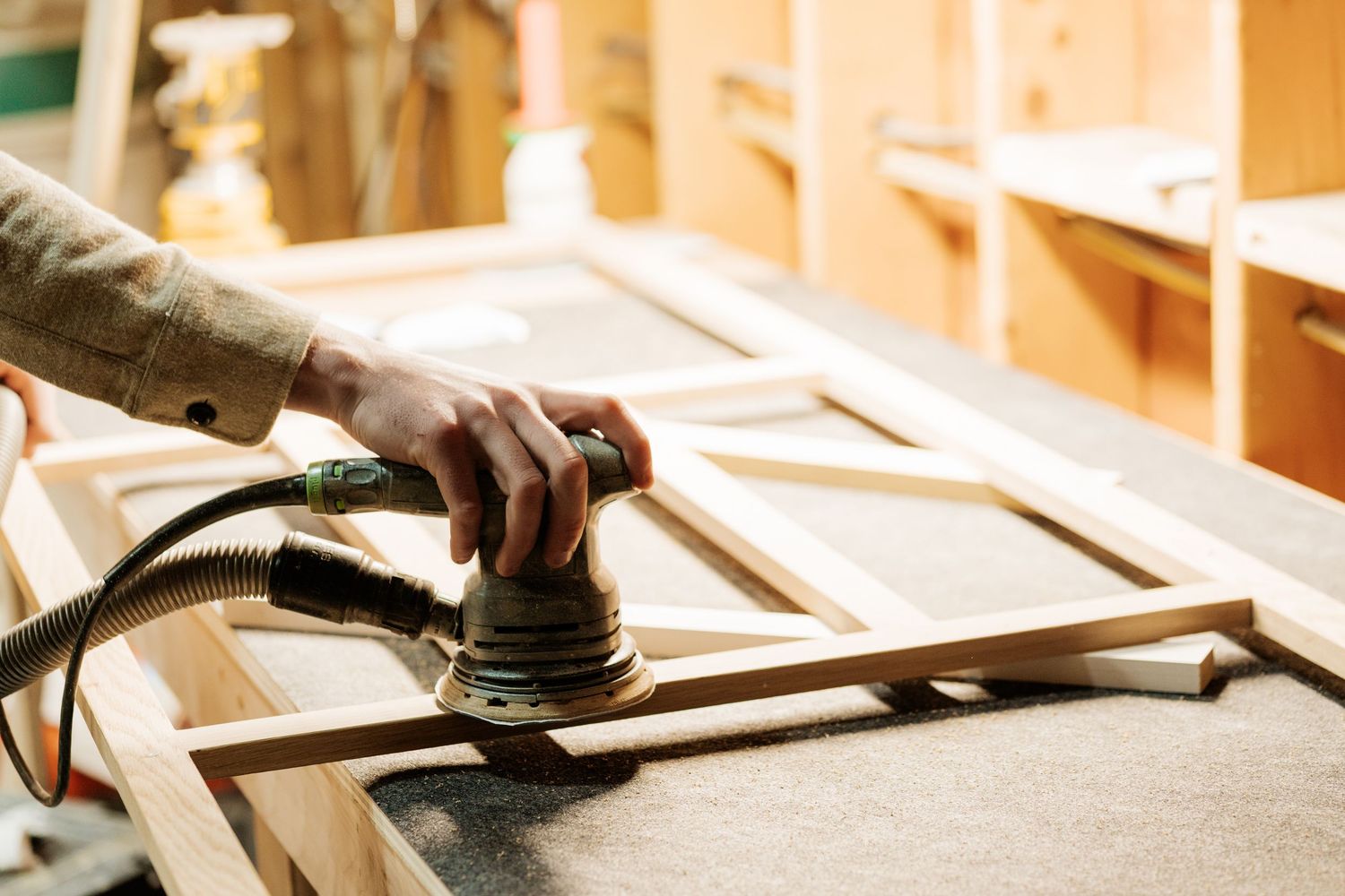 Craftsman sanding wooden furniture components in workshop setting.
