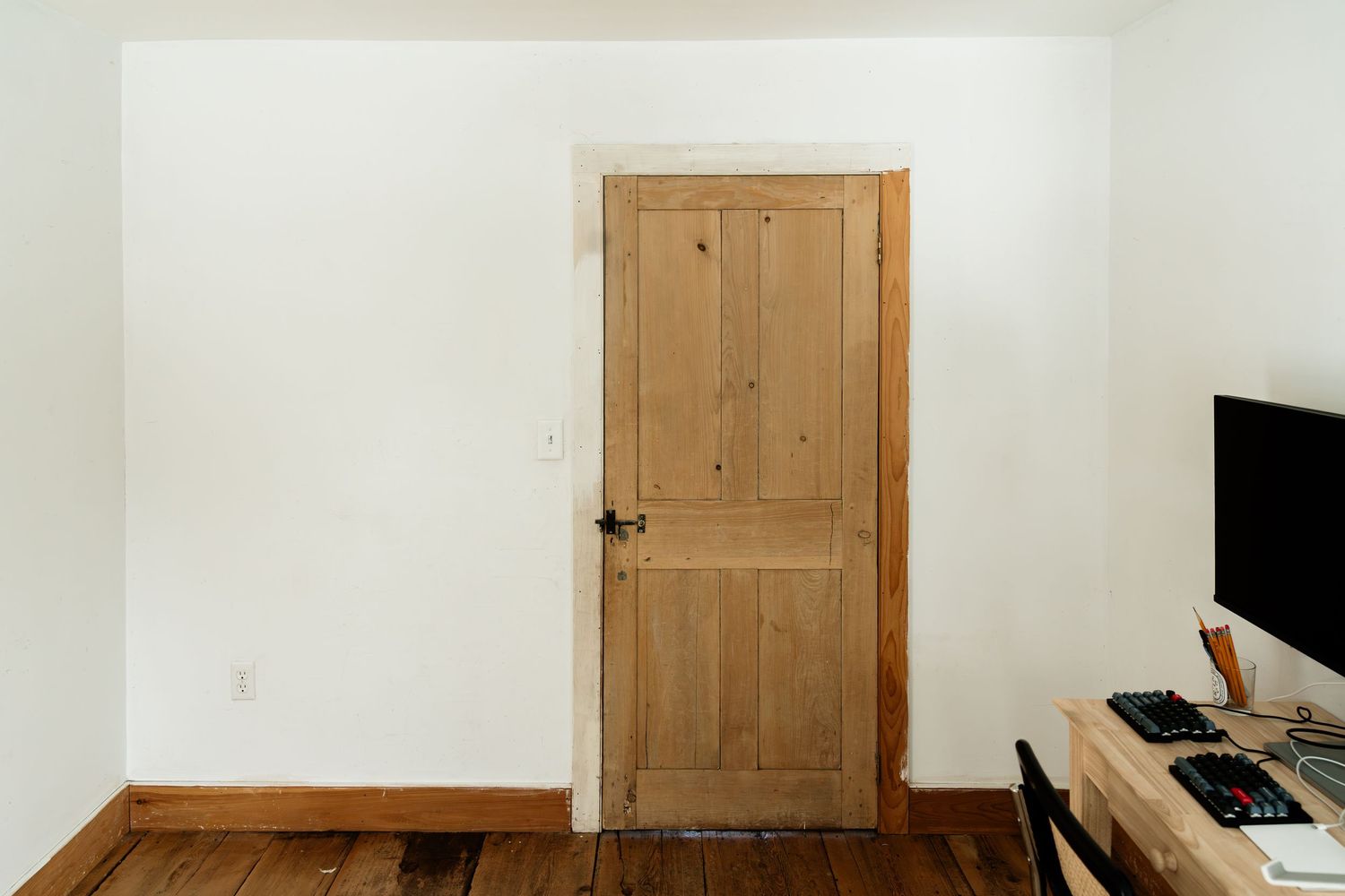 Natural wood door with vertical panels in white room with hardwood flooring.