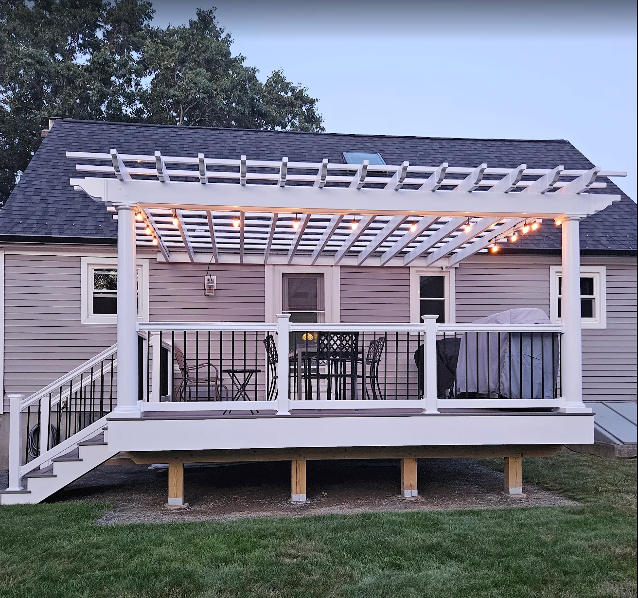Large deck with white pergola and railing extends across the back of a gray house.